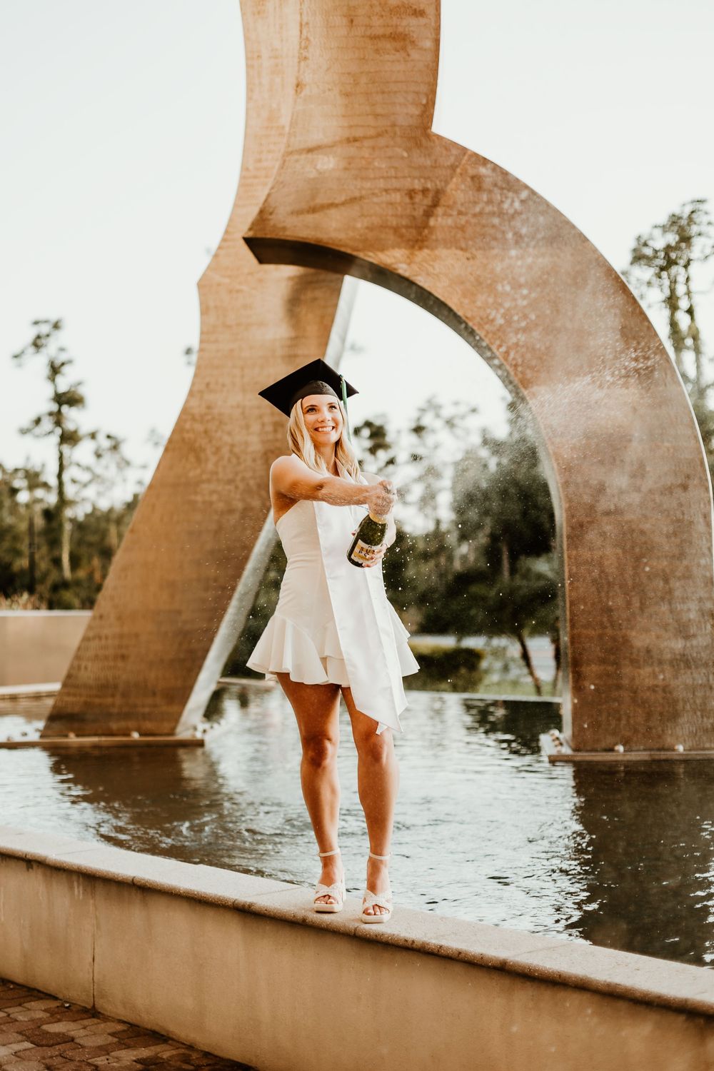 A person stands near illuminated stone archways over water during sunset.