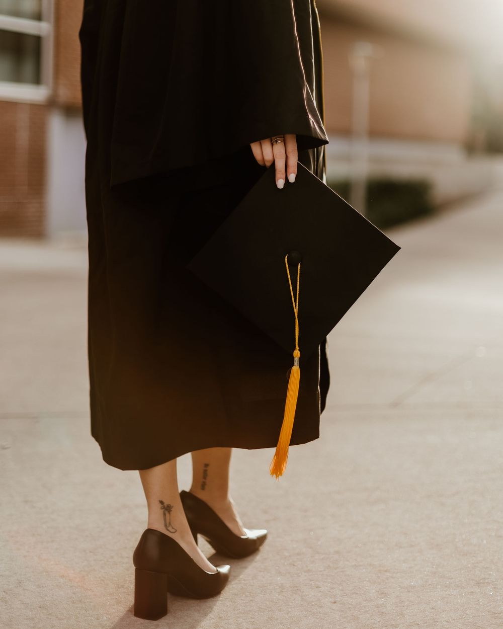 Graduate in black cap and gown shows off heels during graduation photoshoot.
