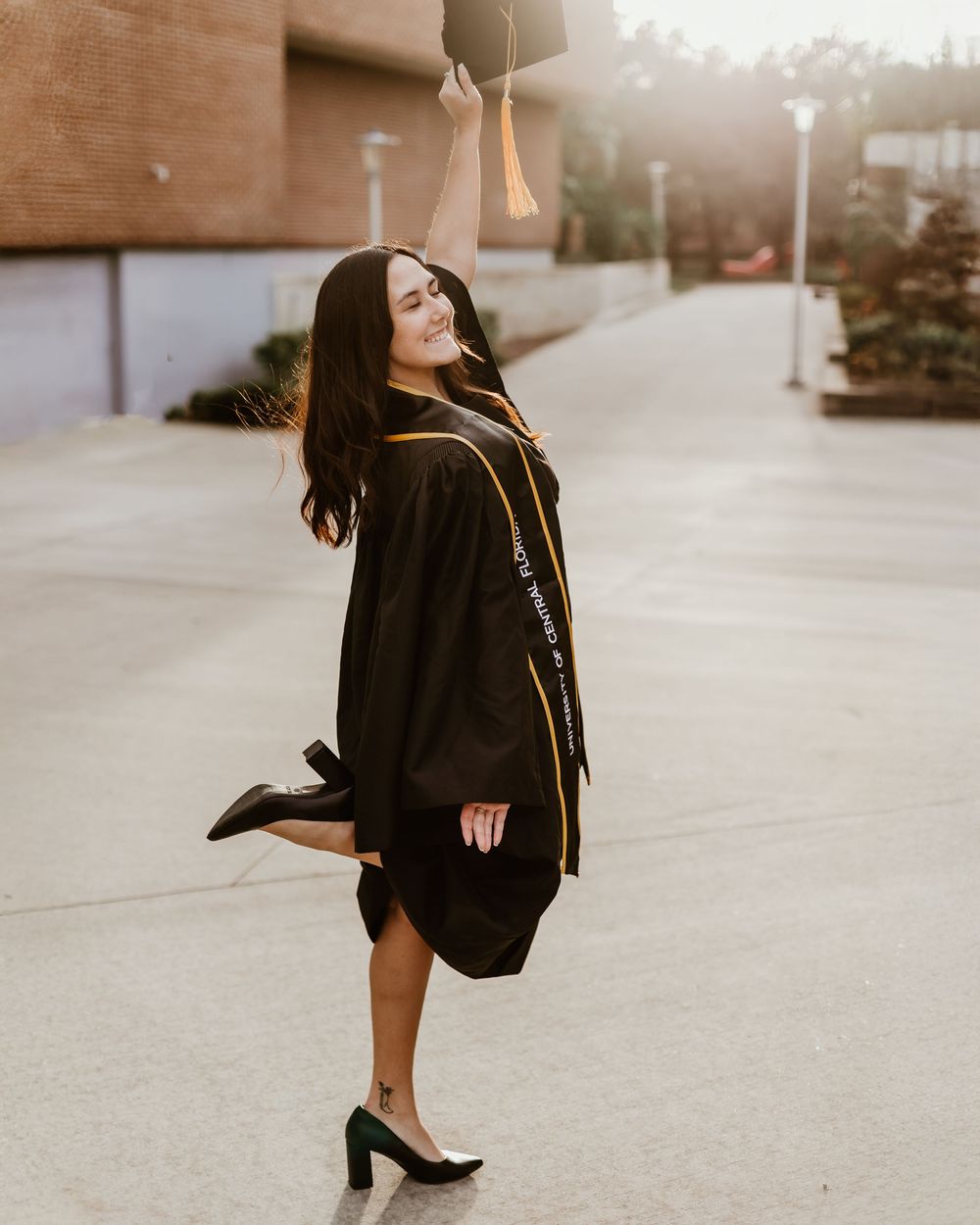 Graduate in black gown strikes playful poses during outdoor photo session.