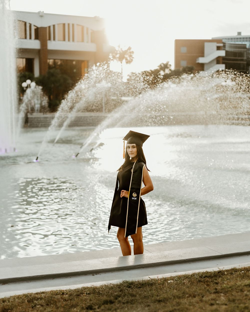 Graduate poses near campus fountain during sunset photoshoot.