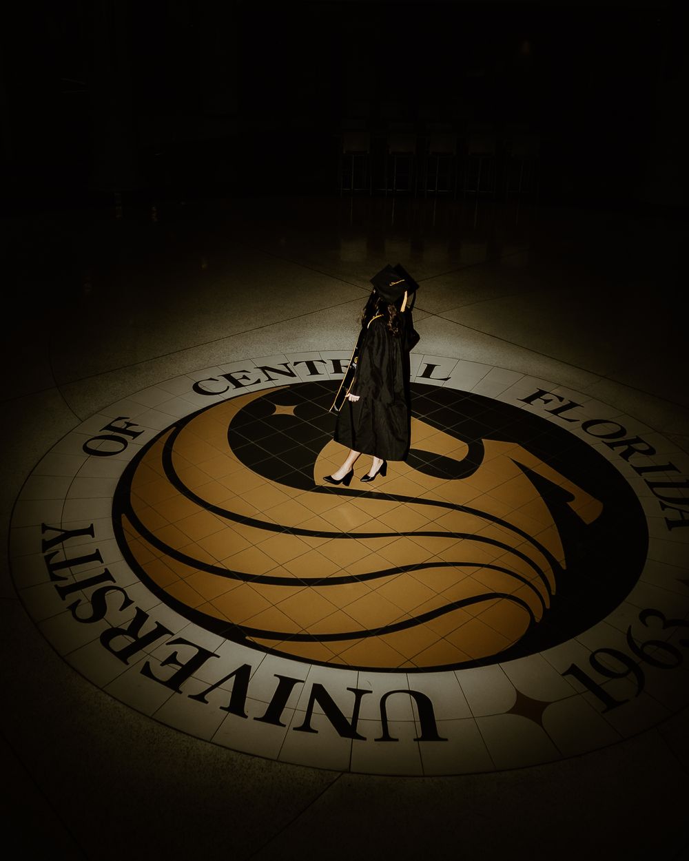 Dramatic spotlight illuminates graduate standing on university seal.