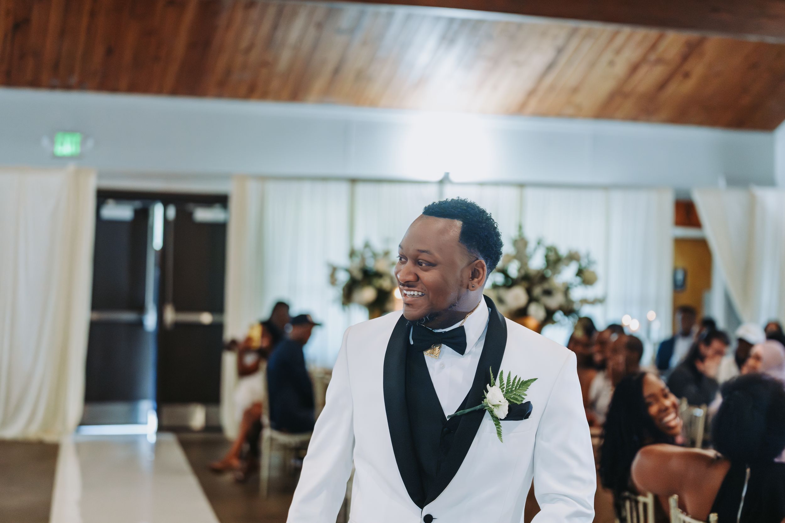 A man in a white vest and black shirt dances with guests at a wedding reception.