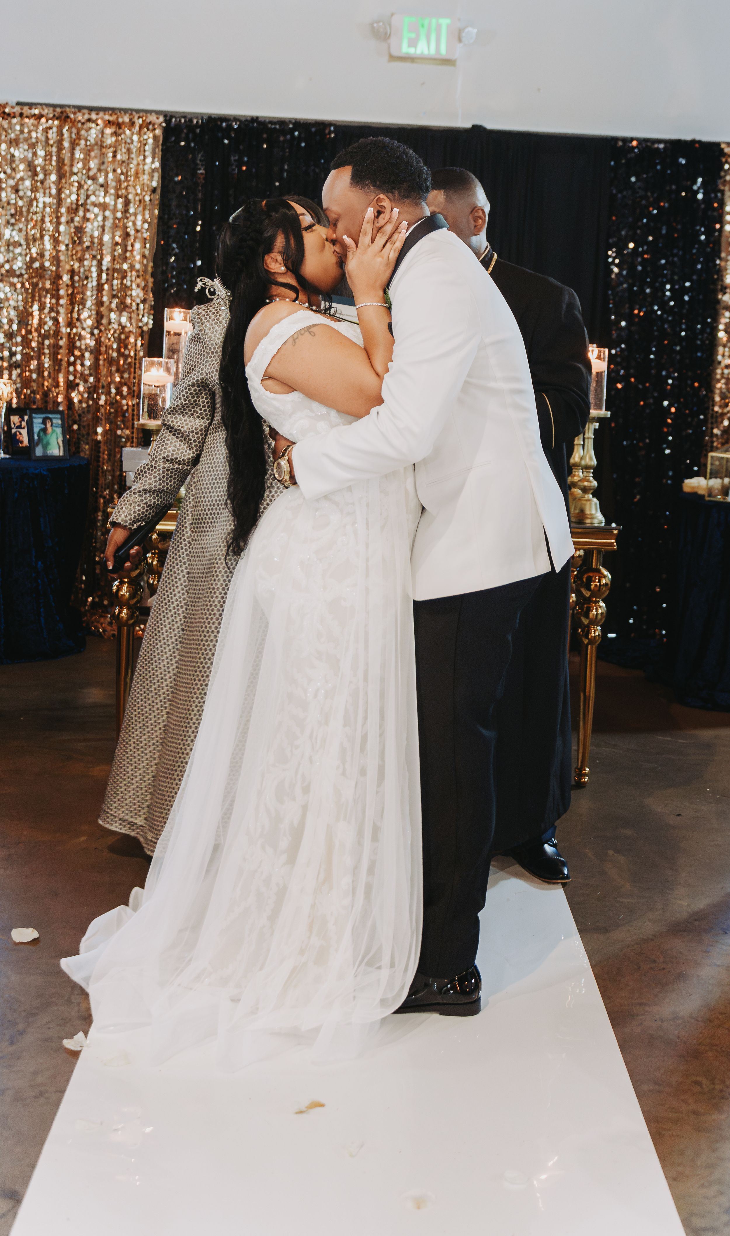 A romantic couple dances together at a wedding reception with a sparkling gold sequin backdrop and twinkling lights.