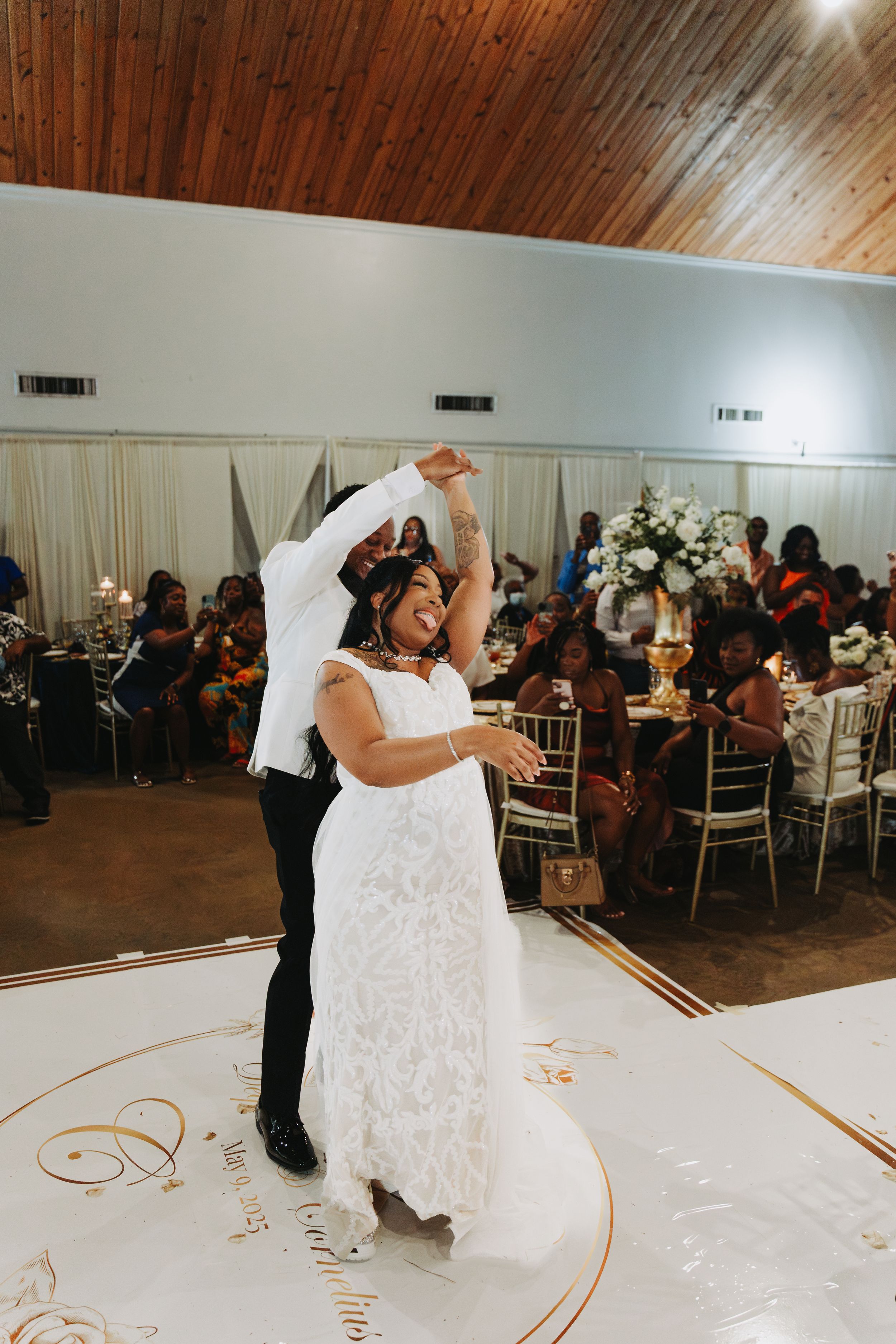 Couple dancing their first dance at wedding reception on decorated white dance floor surrounded by seated guests.