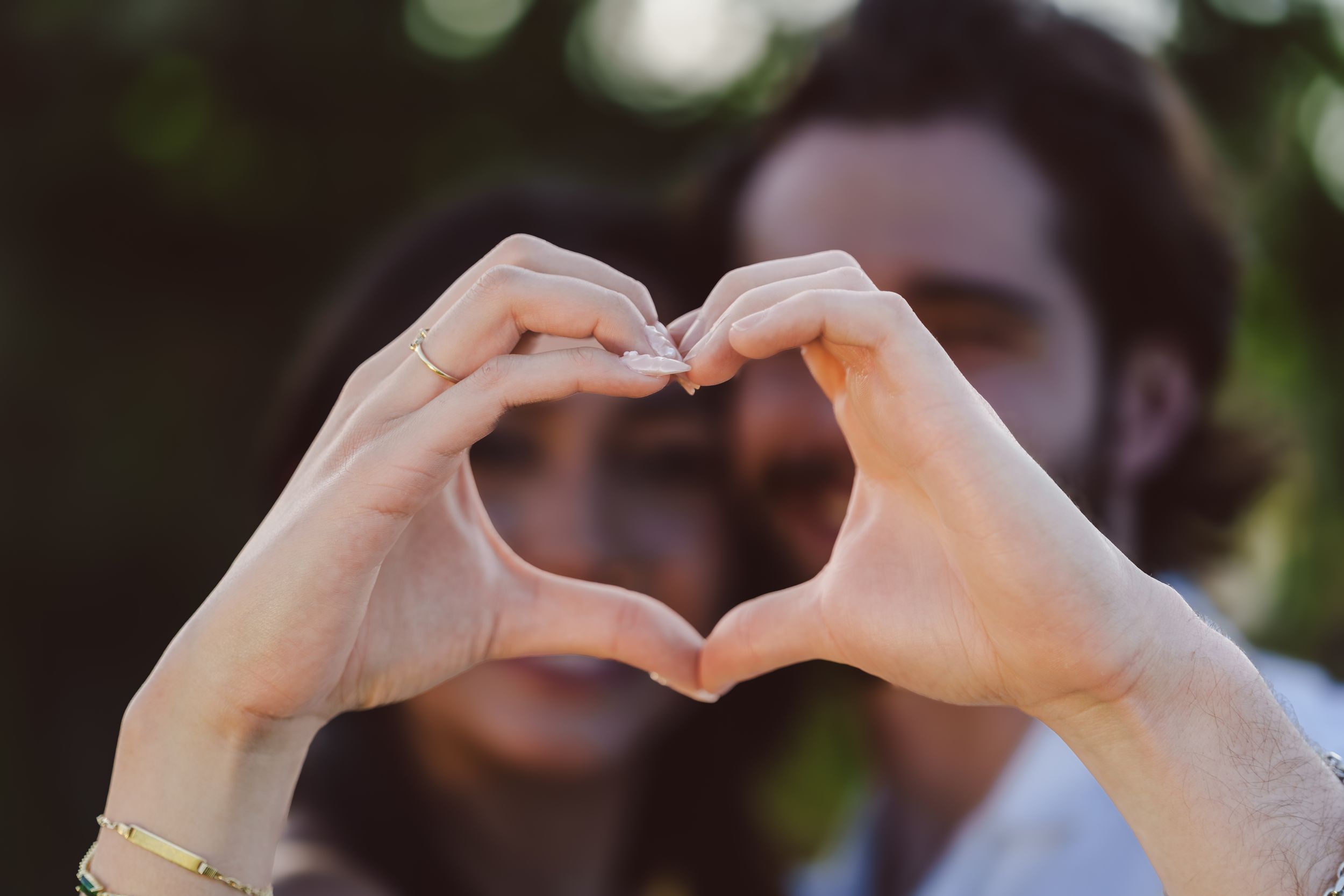 Seven cropped images show hands forming heart shapes against blurred backgrounds.