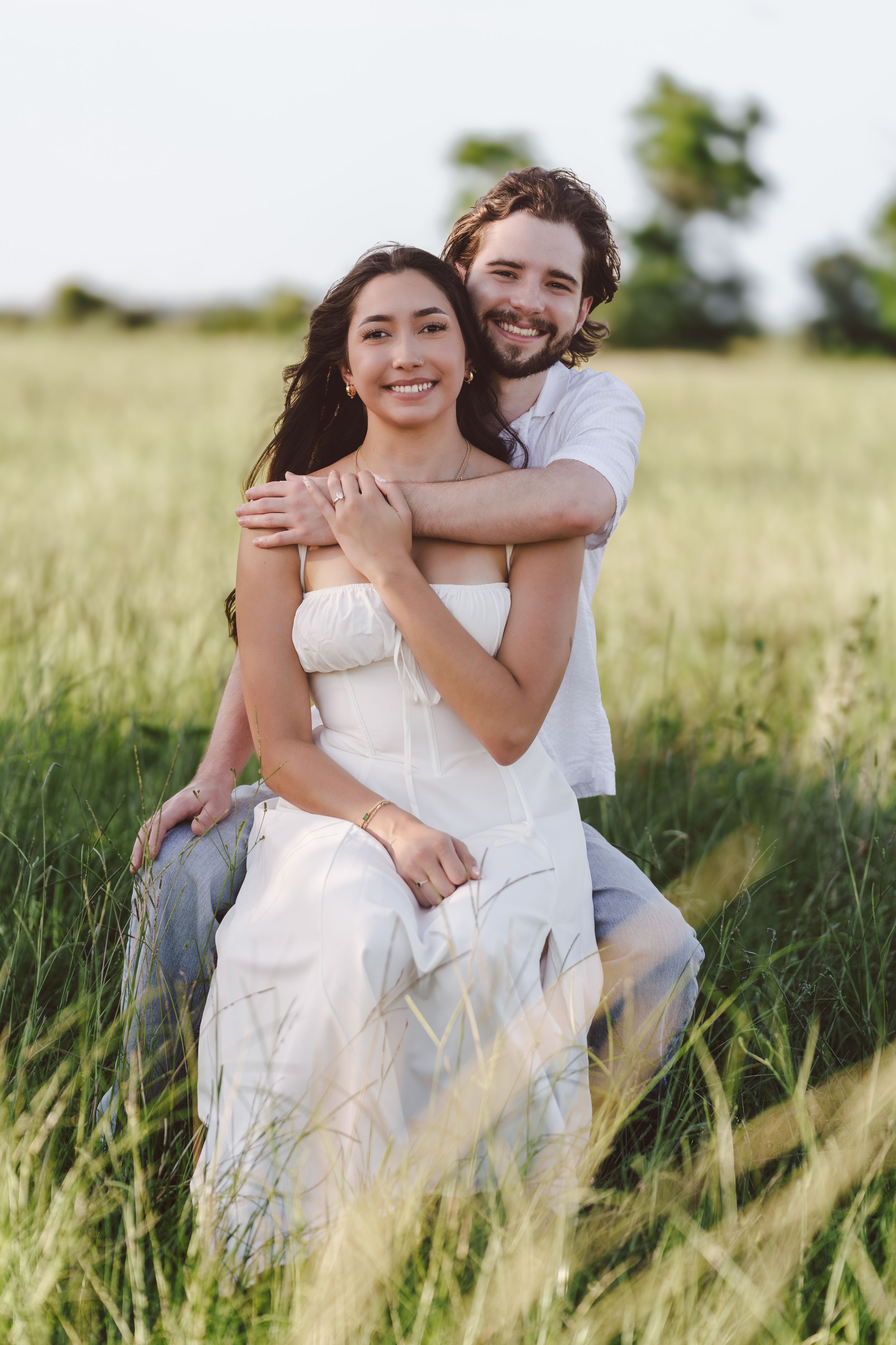 A couple shares an intimate moment while sitting together in tall grass during golden hour.