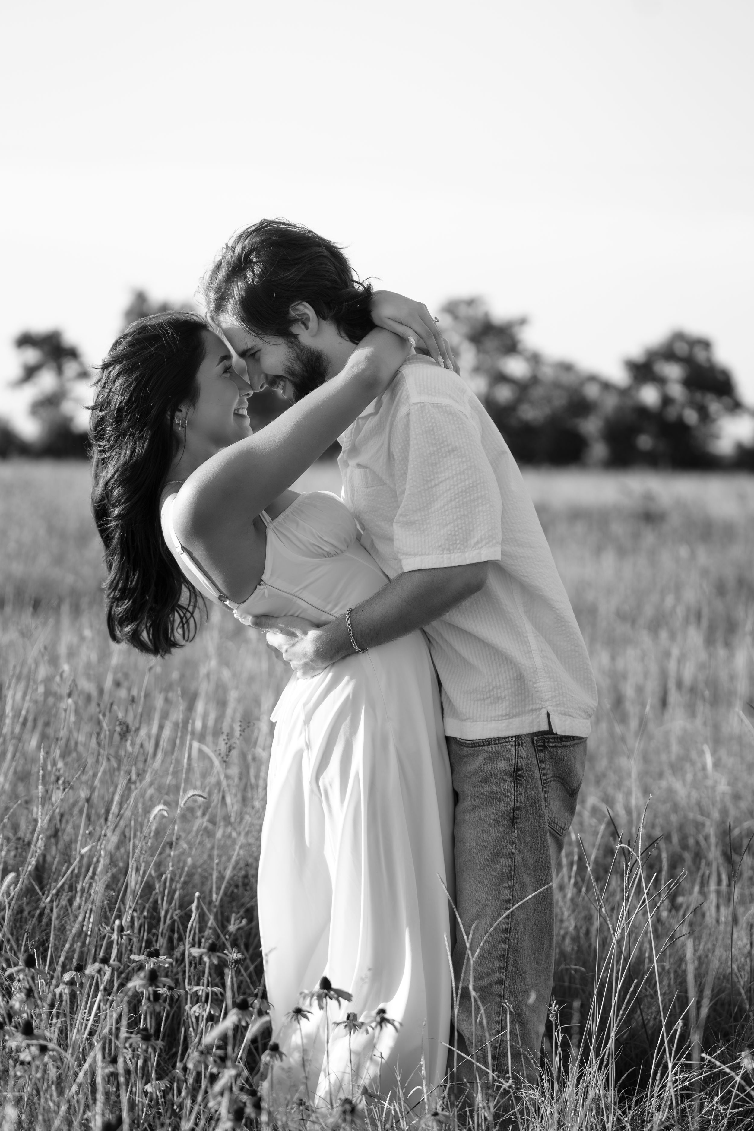 Black and white photo of a romantic couple dancing and embracing in a field of tall grass.