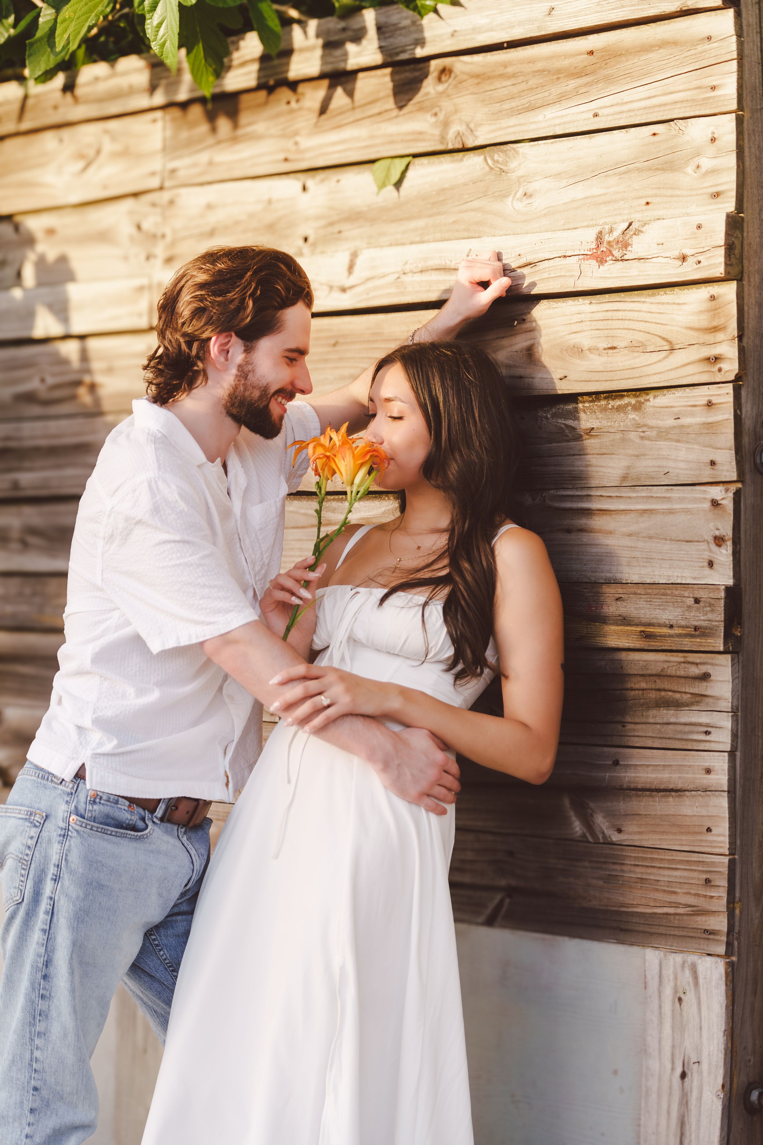 A couple in white clothing share an intimate moment against a rustic wooden wall backdrop.