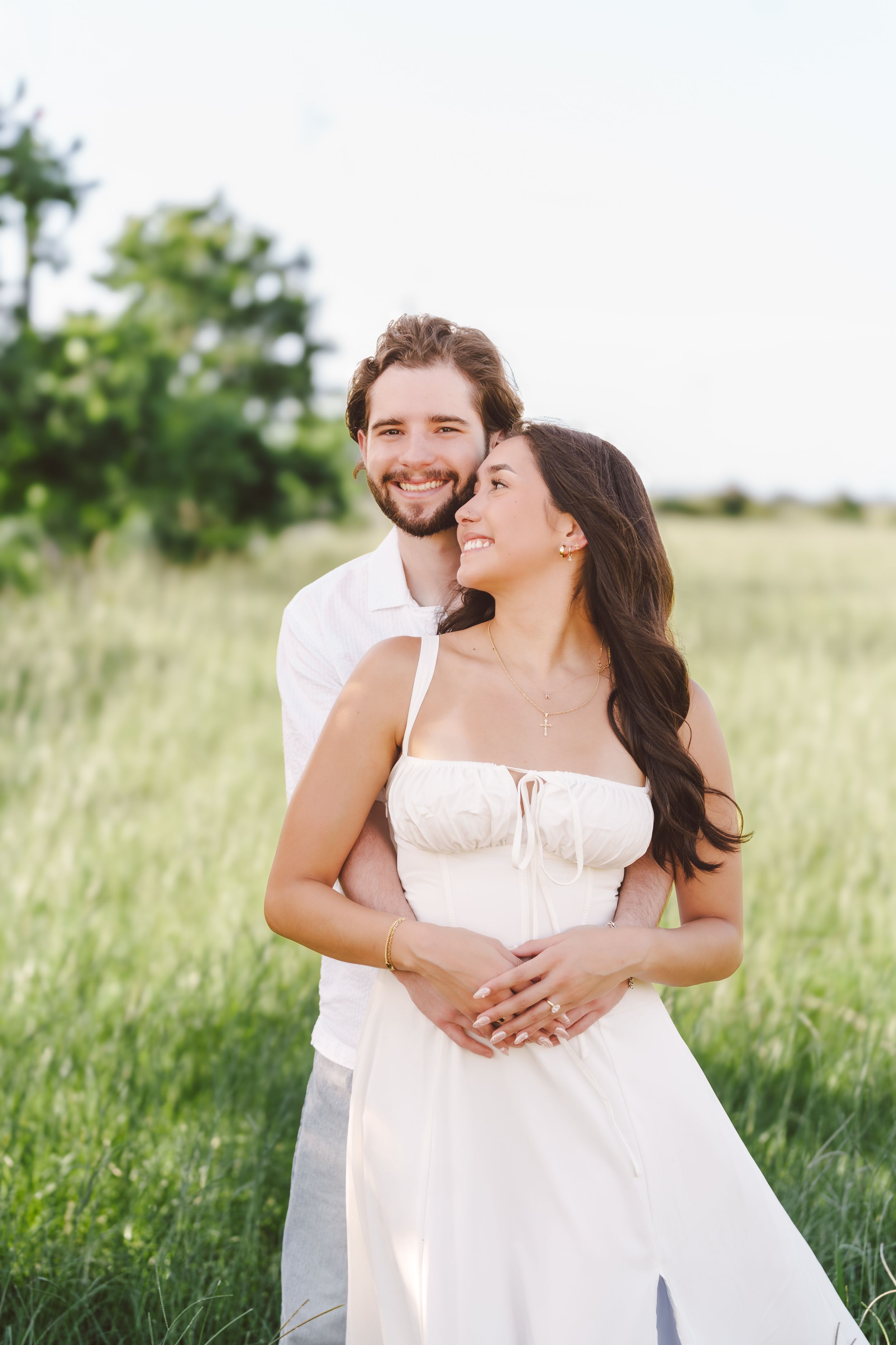 A happy couple embraces in a sunlit meadow wearing white and pink summer outfits.