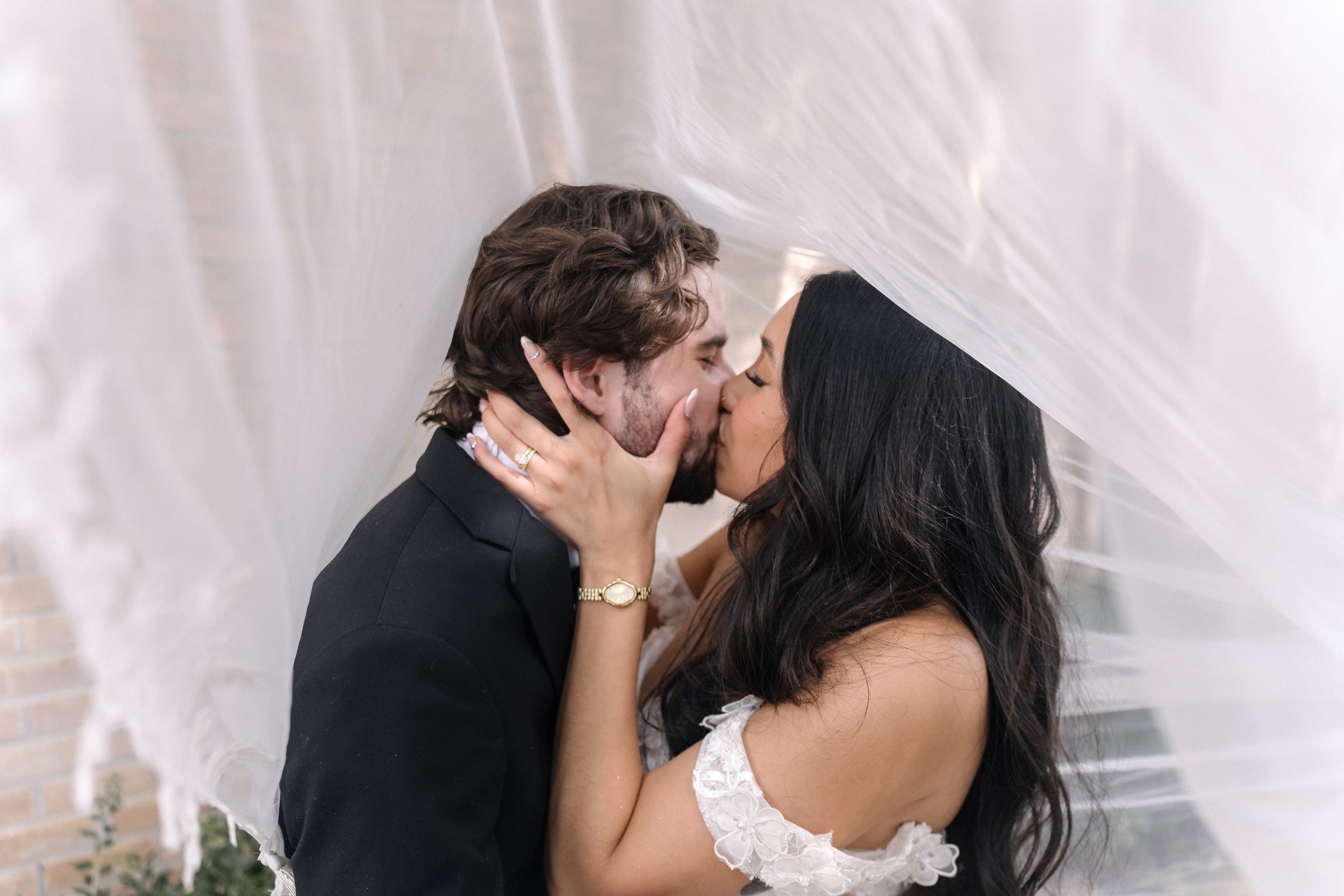 A couple shares a passionate wedding kiss under elegant white drapery during their romantic ceremony.