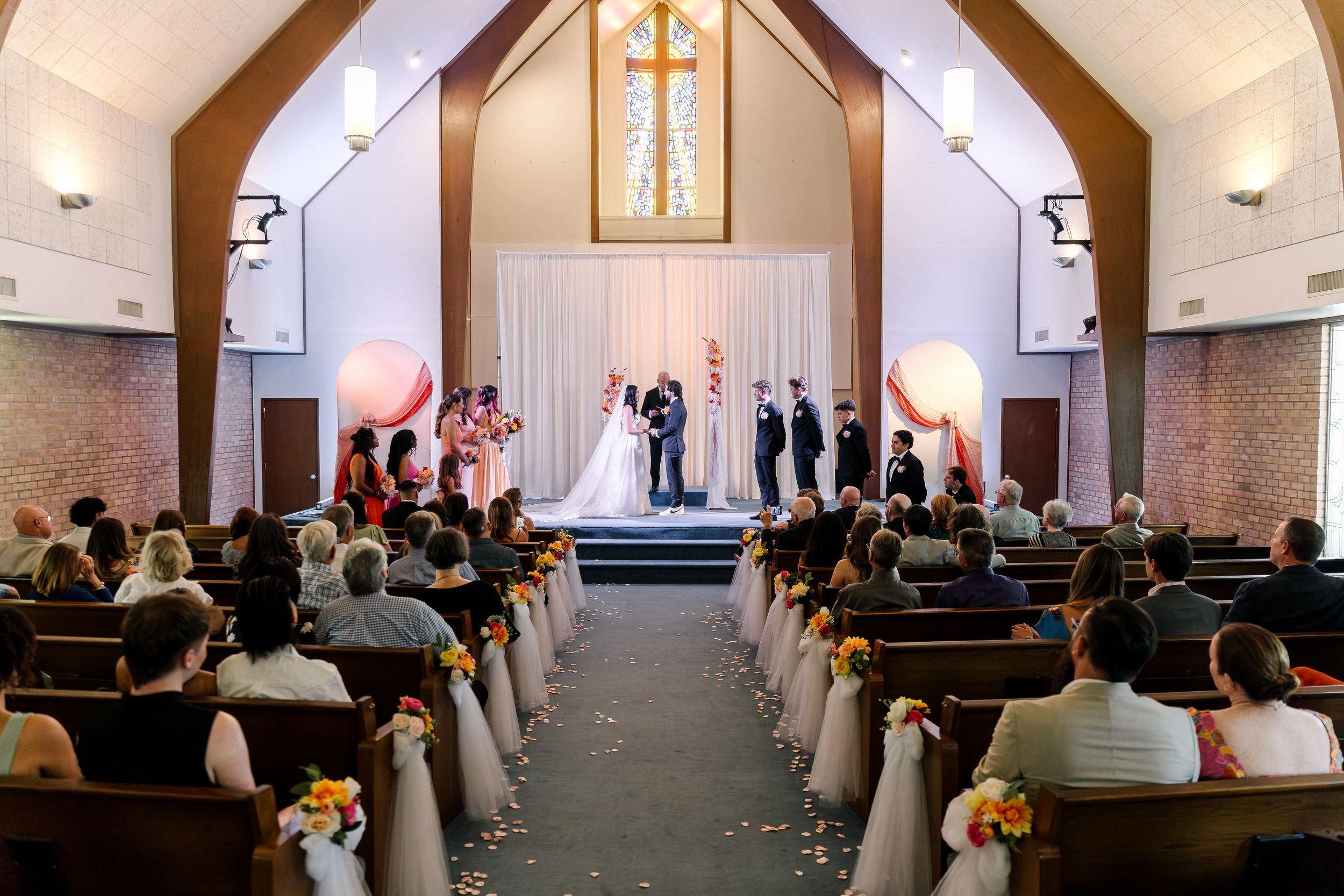A church wedding ceremony showing pews, crosses on walls, and guests gathered in a traditional chapel setting.