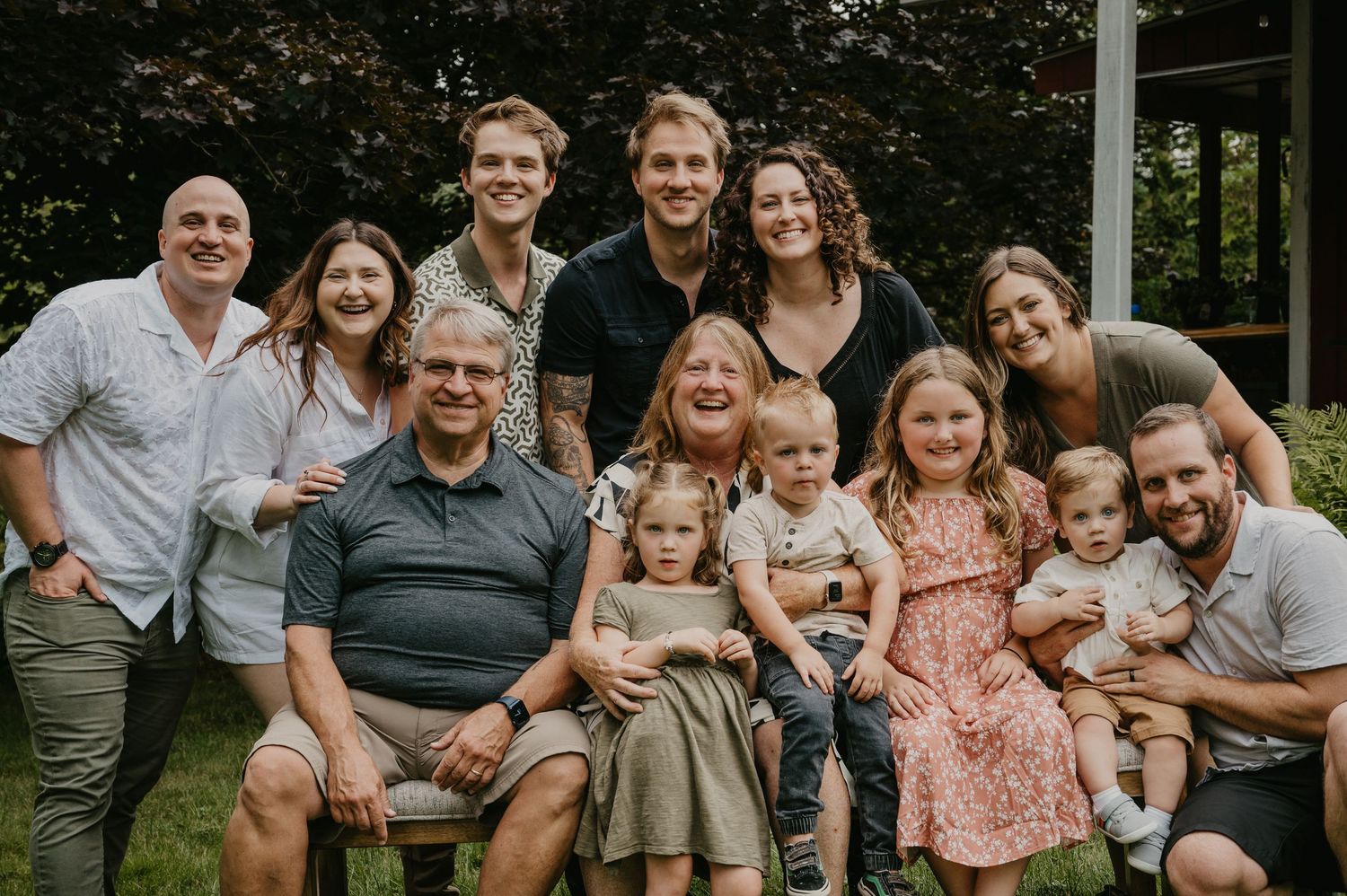 Large multigenerational family posing together outdoors in a lush green garden setting.