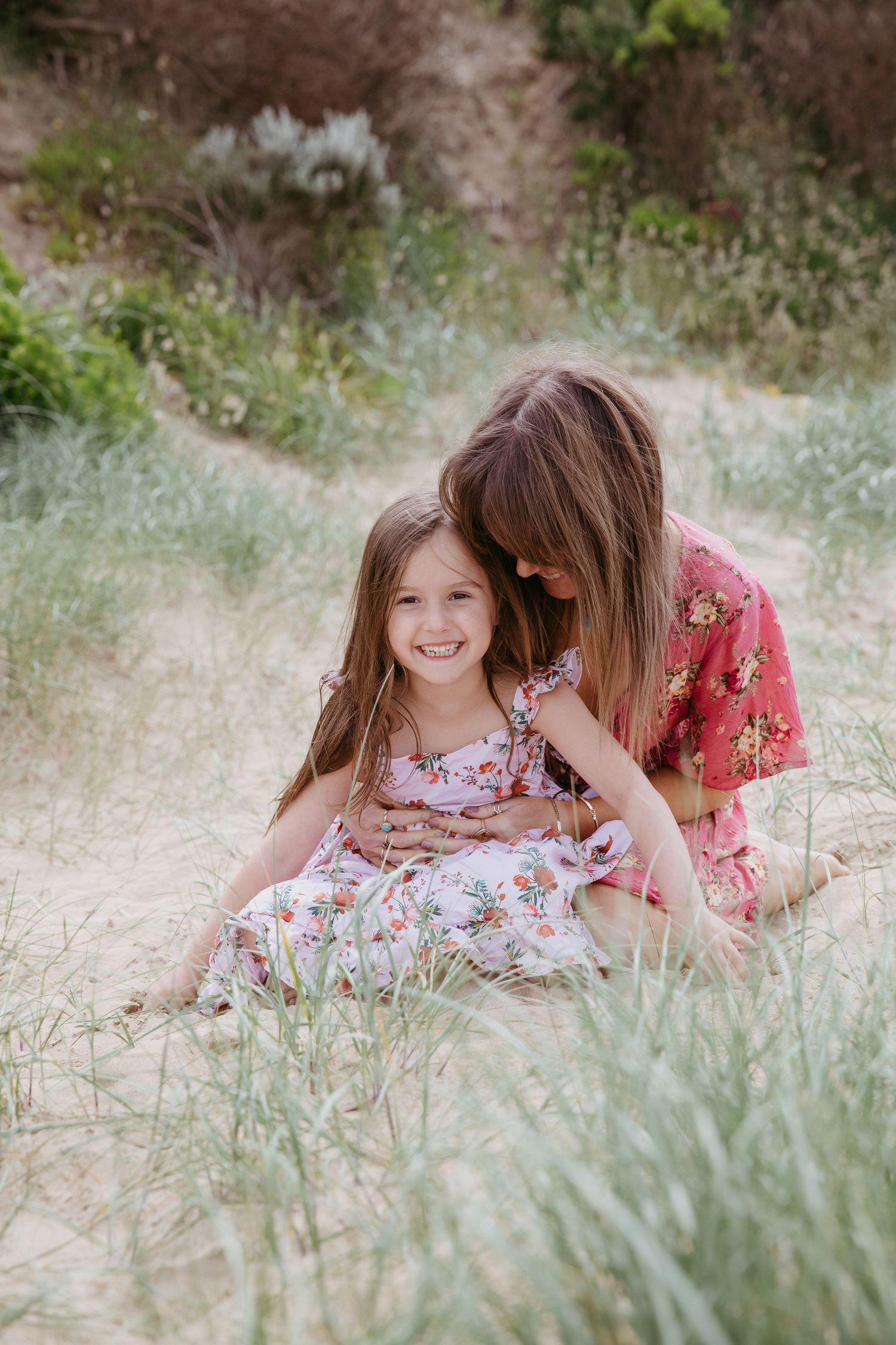 Mum sitting cuddling smiling daughter on the sand in Ocean Grove