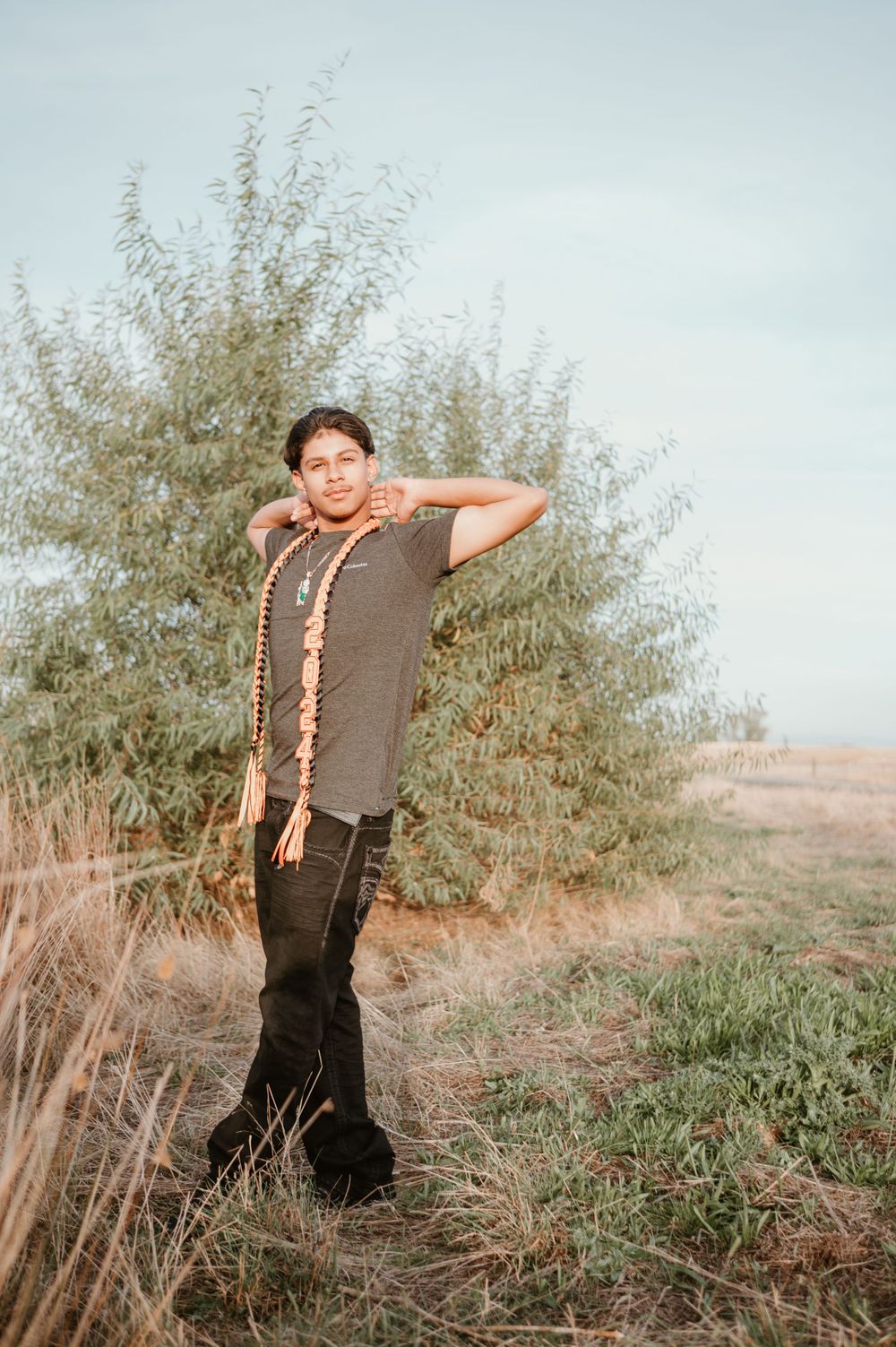 A graduate poses playfully in a field wearing orange graduation stoles.