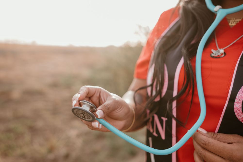 Close-up of a graduate holding a light blue stethoscope against an orange nursing graduation stole.