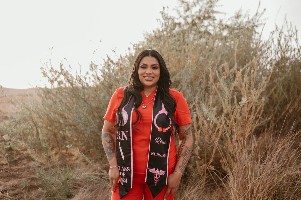 Graduate in a bright red dress poses outdoors against natural desert brush and foliage.