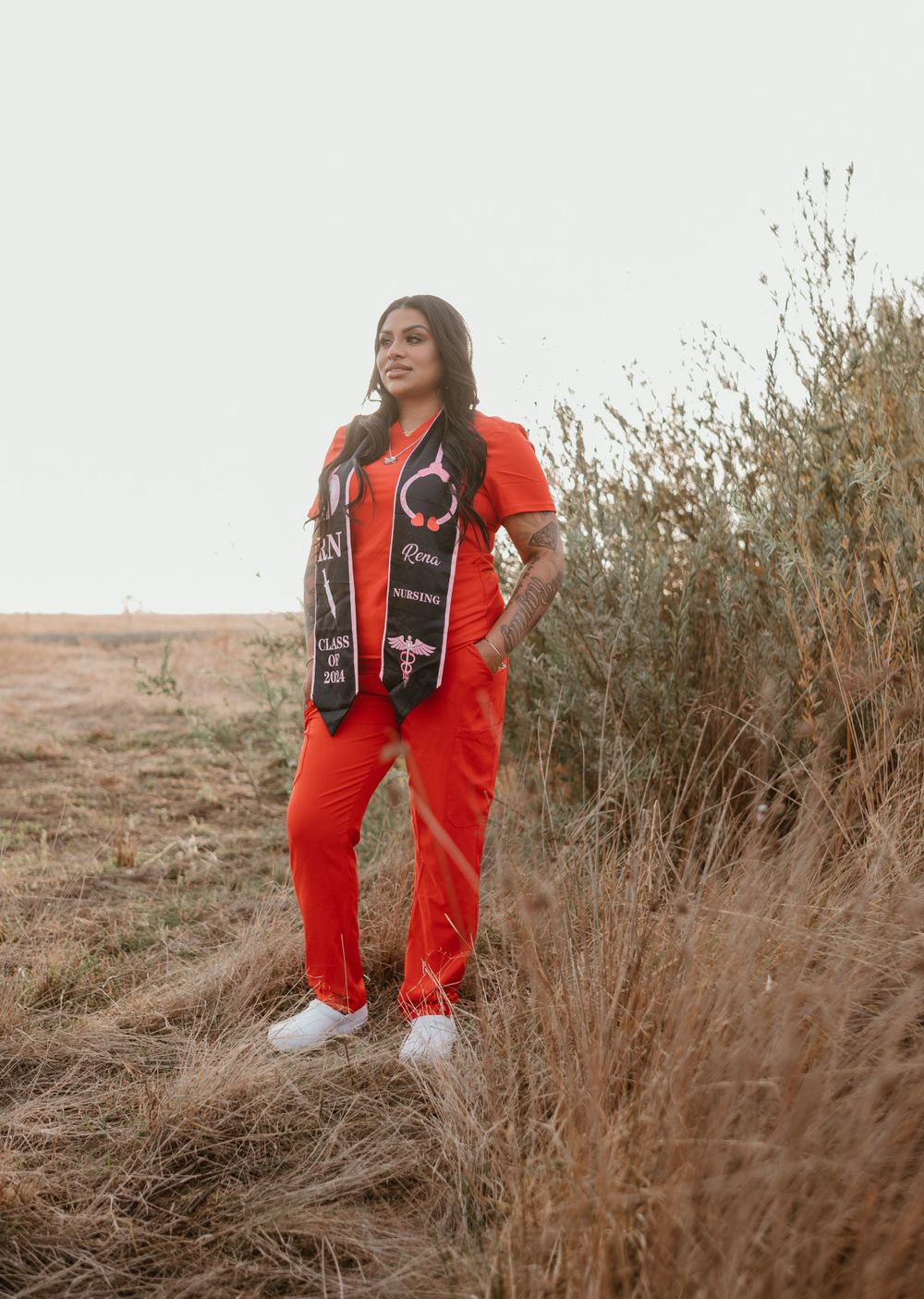 Graduate wearing red dress sits casually on ground surrounded by desert plants.