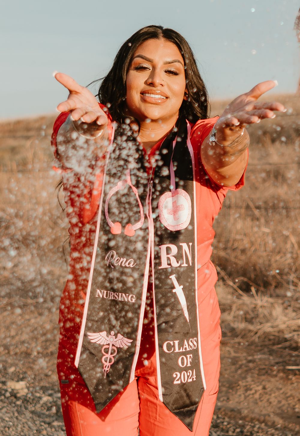 Graduate celebrates by tossing confetti while wearing nursing graduation stole outdoors.