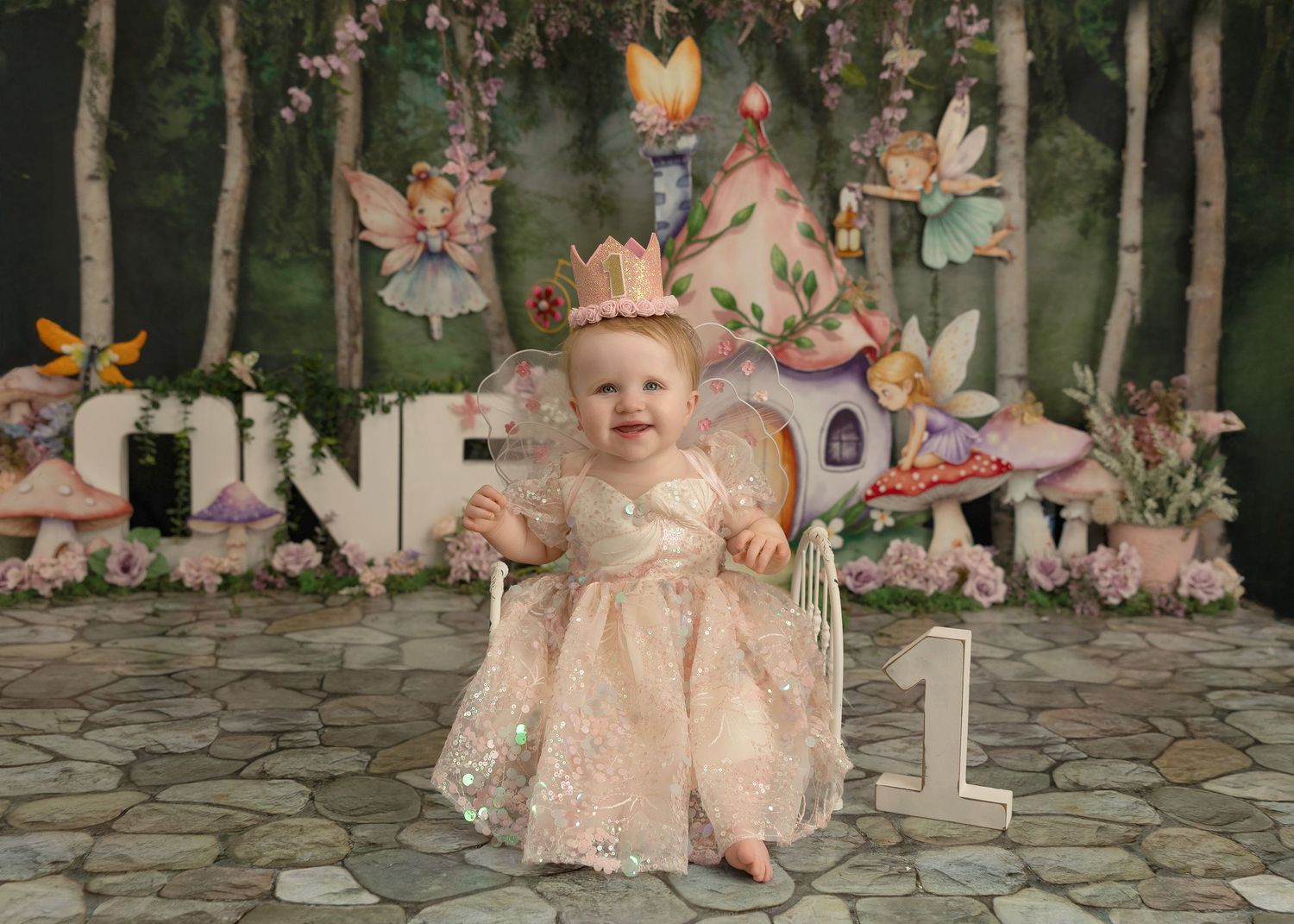 Enchanted woodland themed first birthday photo setup with fairy decorations, mushrooms and stone floor backdrop.