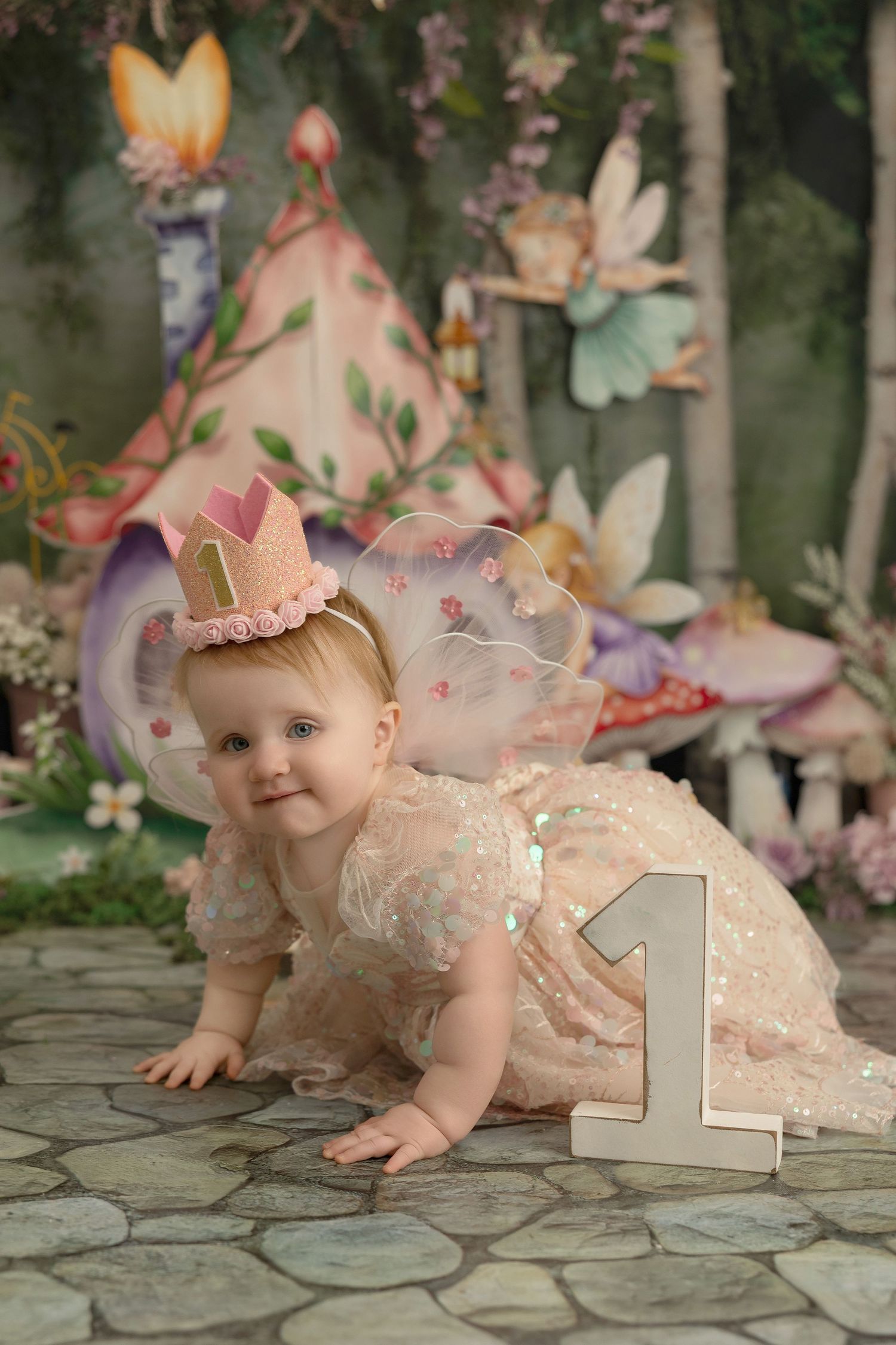 Enchanting first birthday photo setup with pink teepee, butterfly decorations, and fairy tale woodland theme on stone floor.