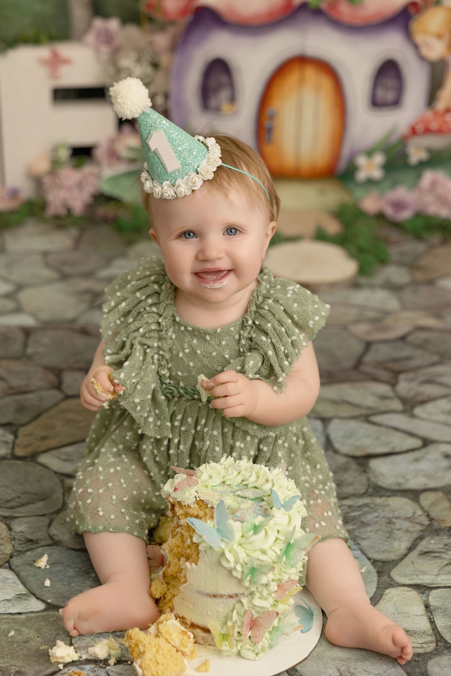Baby wearing mint green polka dot dress sitting on stone patio during cake smash photo session.