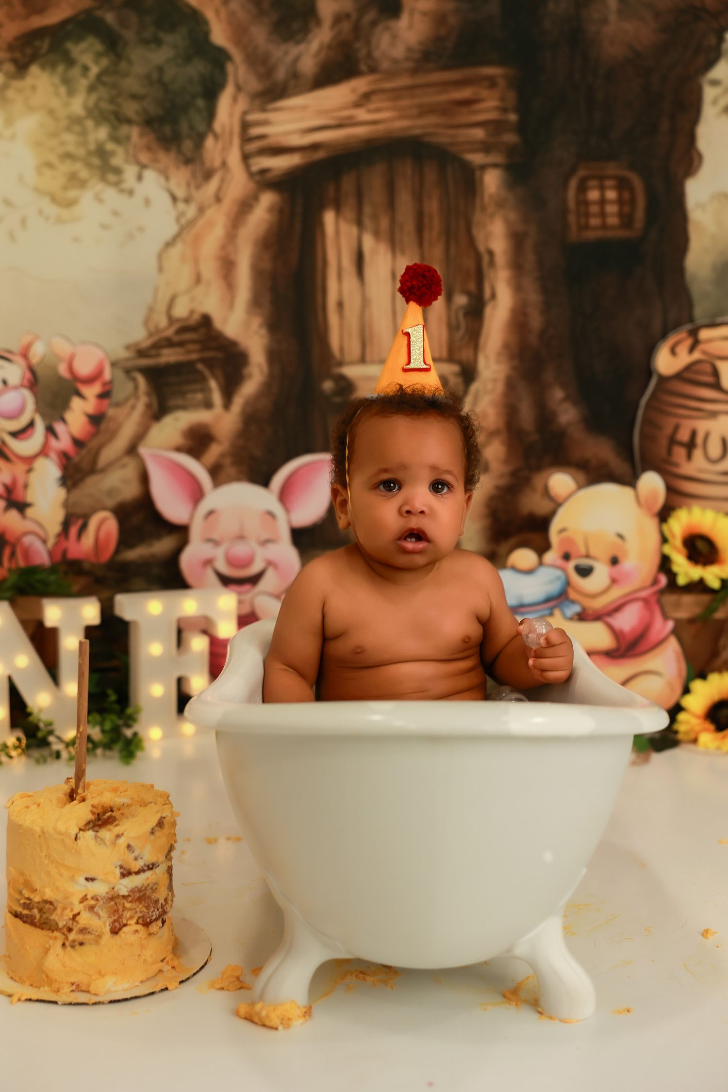 Baby sits in white bowl during cake smash photo session with enchanted forest themed background.