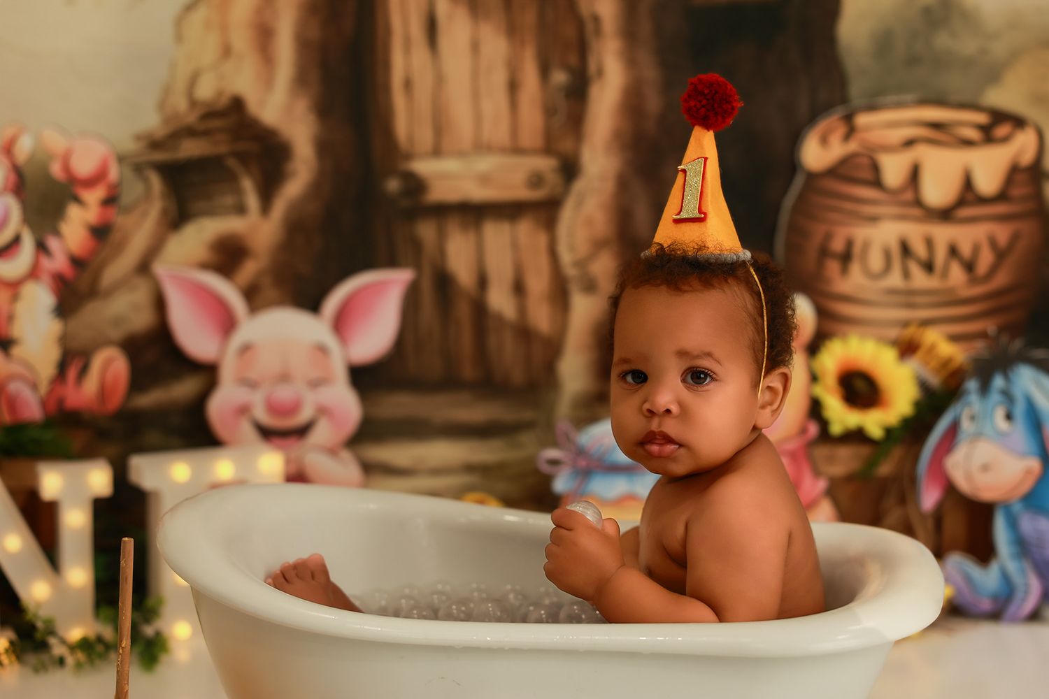 A rustic honey-themed photo session setup with plush toys, wooden decorations, and a small bathtub against a brown backdrop.