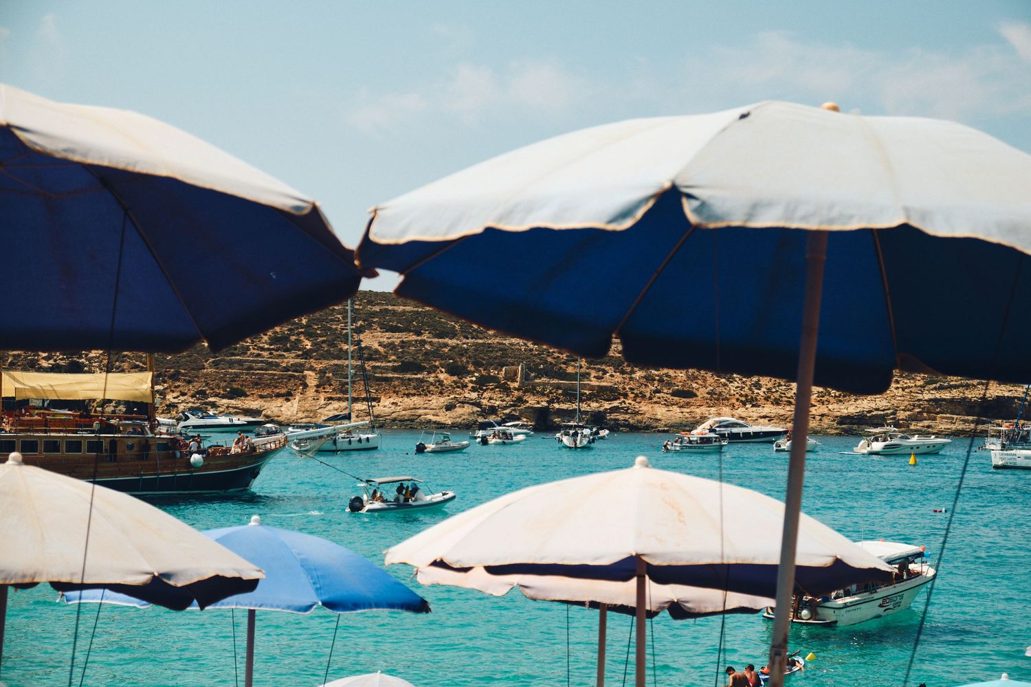 Blue and white beach umbrellas shading boats in crystal clear Mediterranean waters.