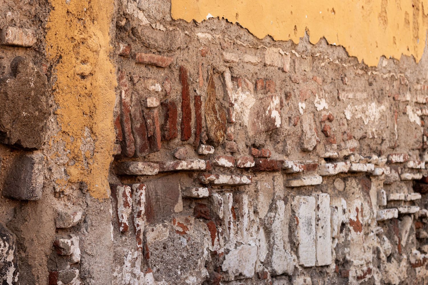 Weathered yellow wall texture showing peeling paint and exposed brick.