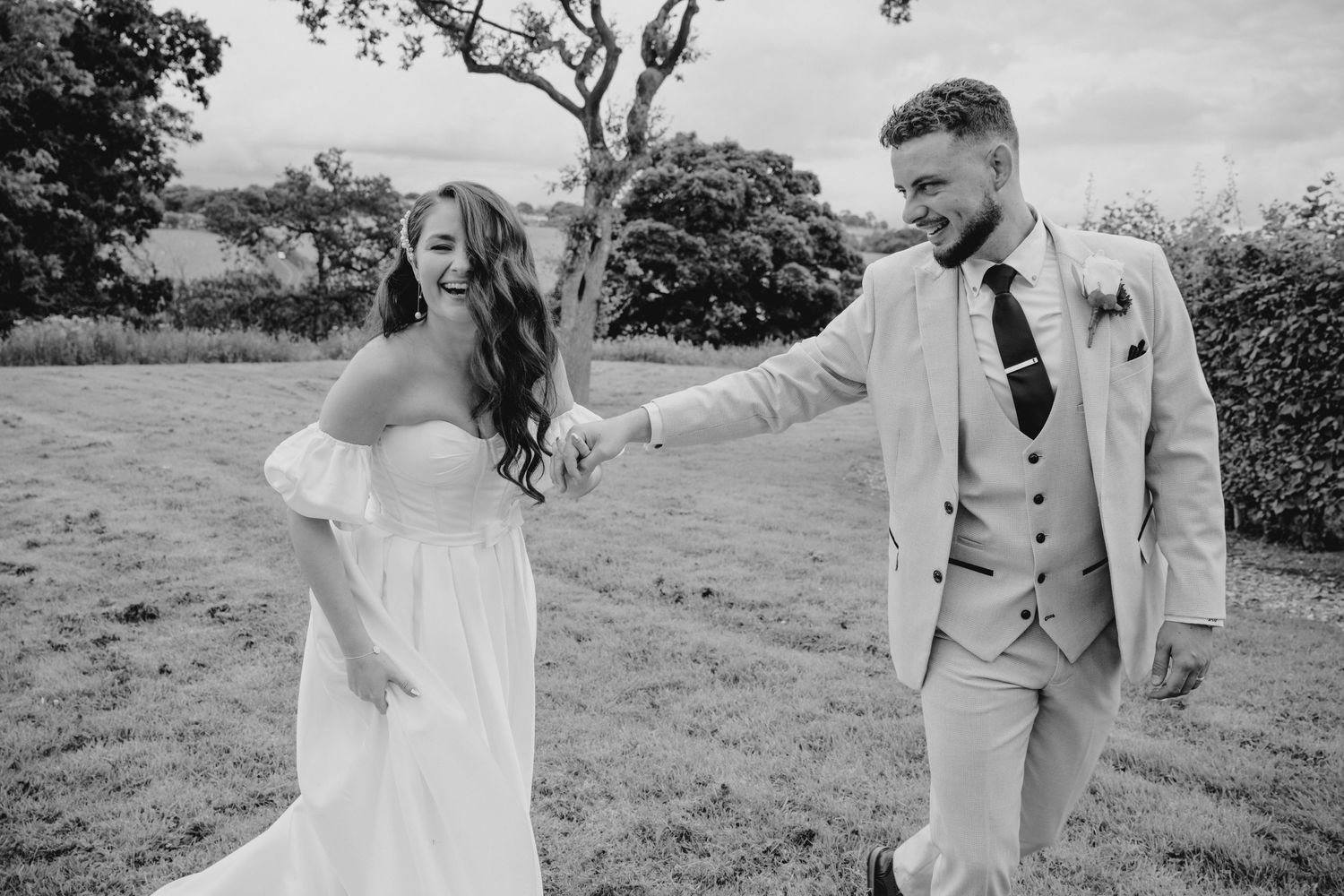 Black and white photo of a couple sharing a playful moment in an open field.