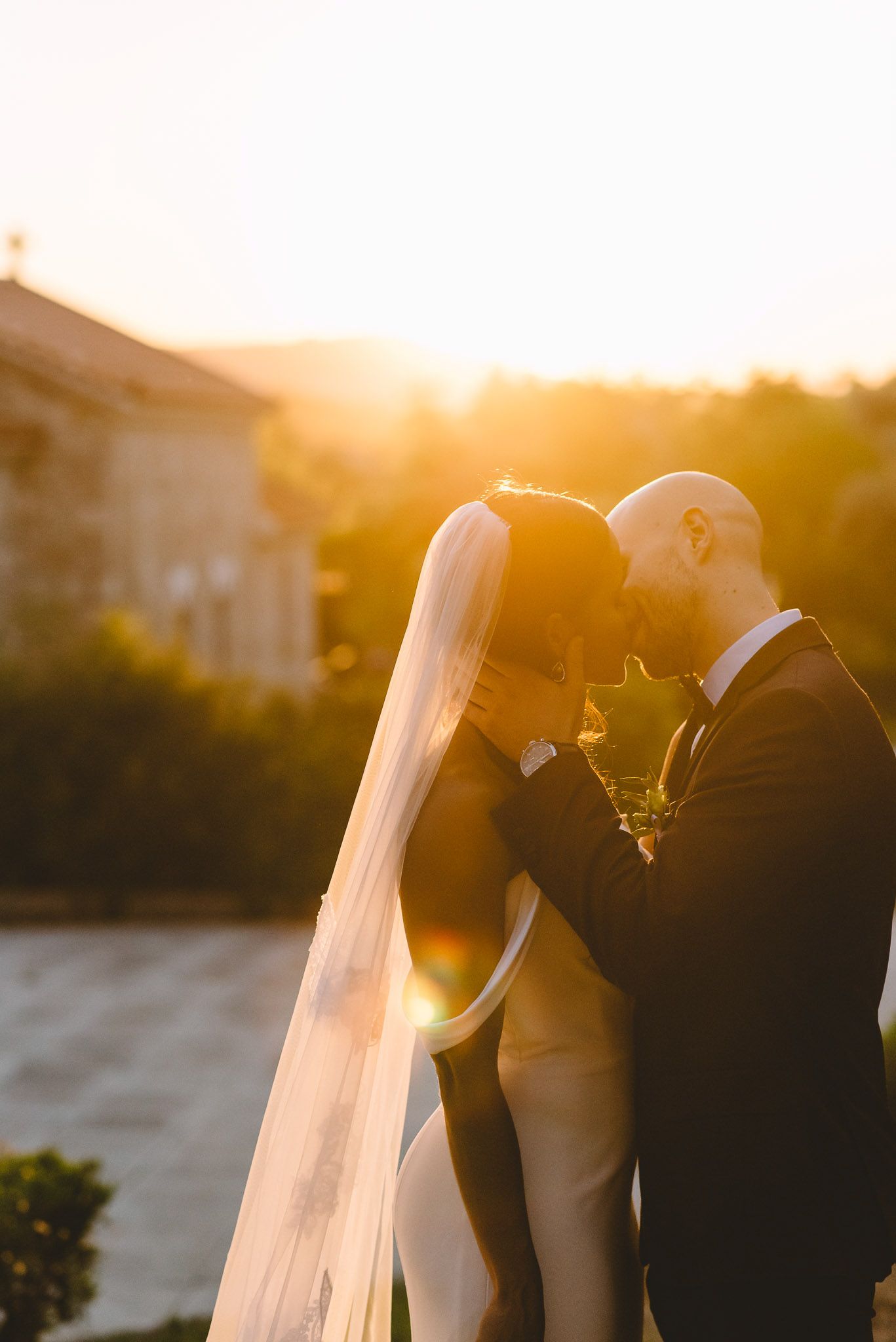Silhouetted couple sharing an intimate moment at sunset with a long flowing wedding veil.