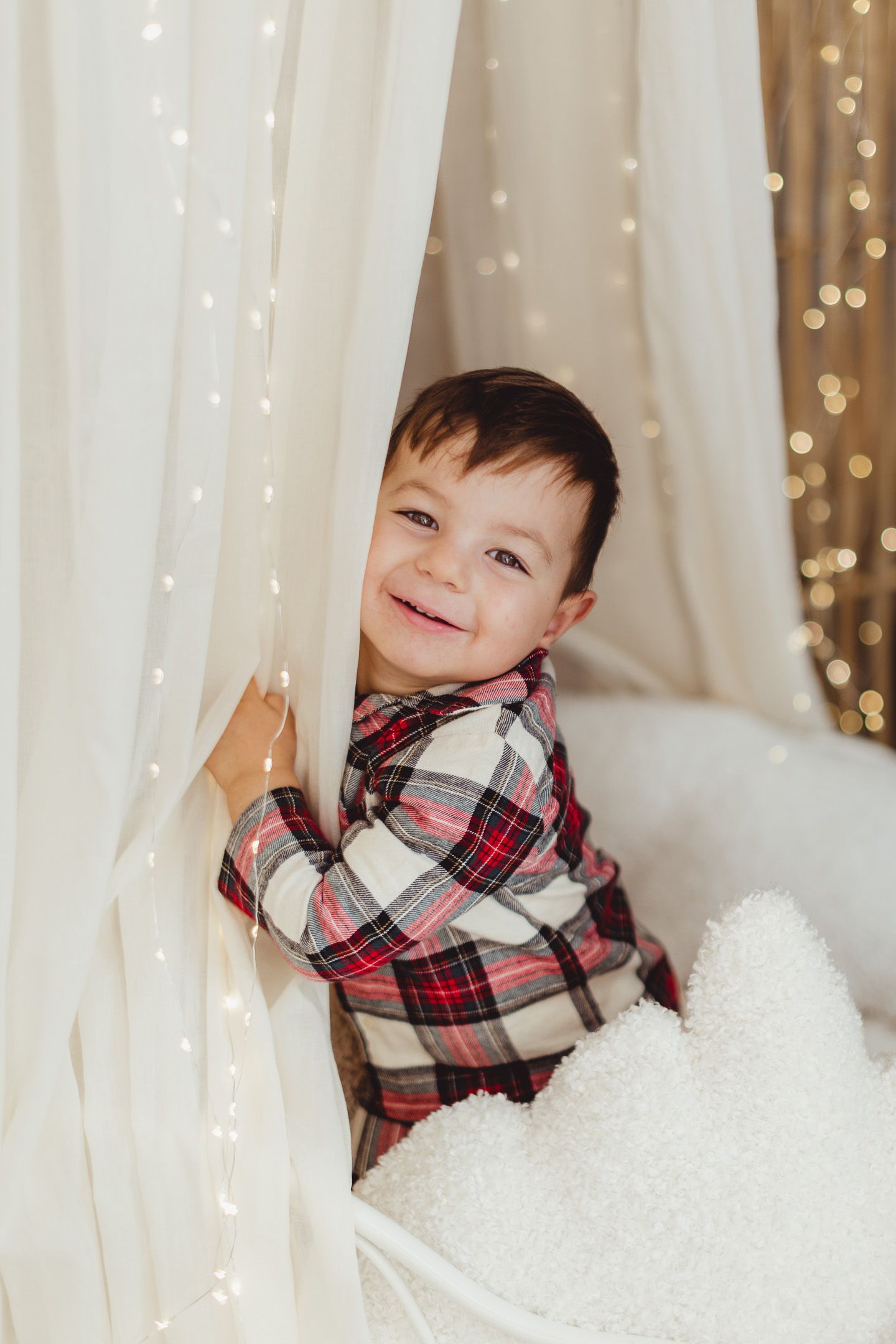 Holiday photo session with white curtains and twinkling lights backdrop.
