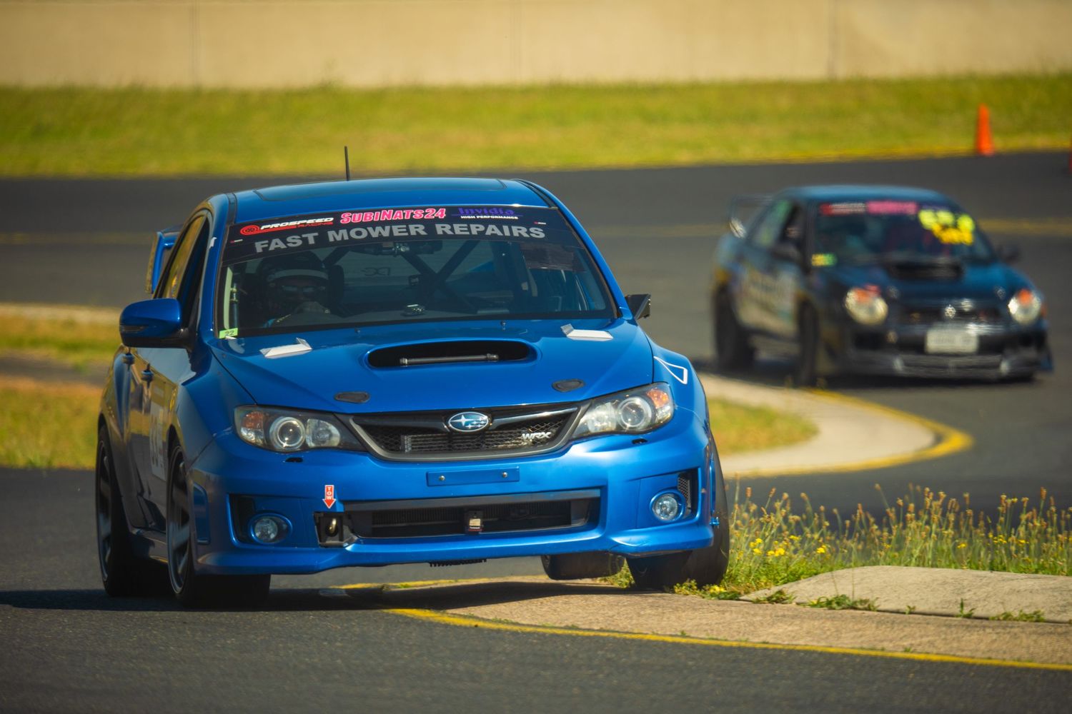 Blue Subaru WRX STI racing on track with another car following behind.