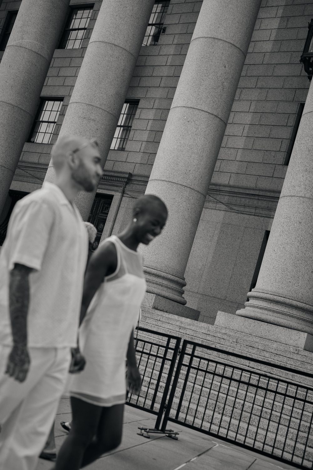 Two people in white outfits walking past classical stone columns of a building.