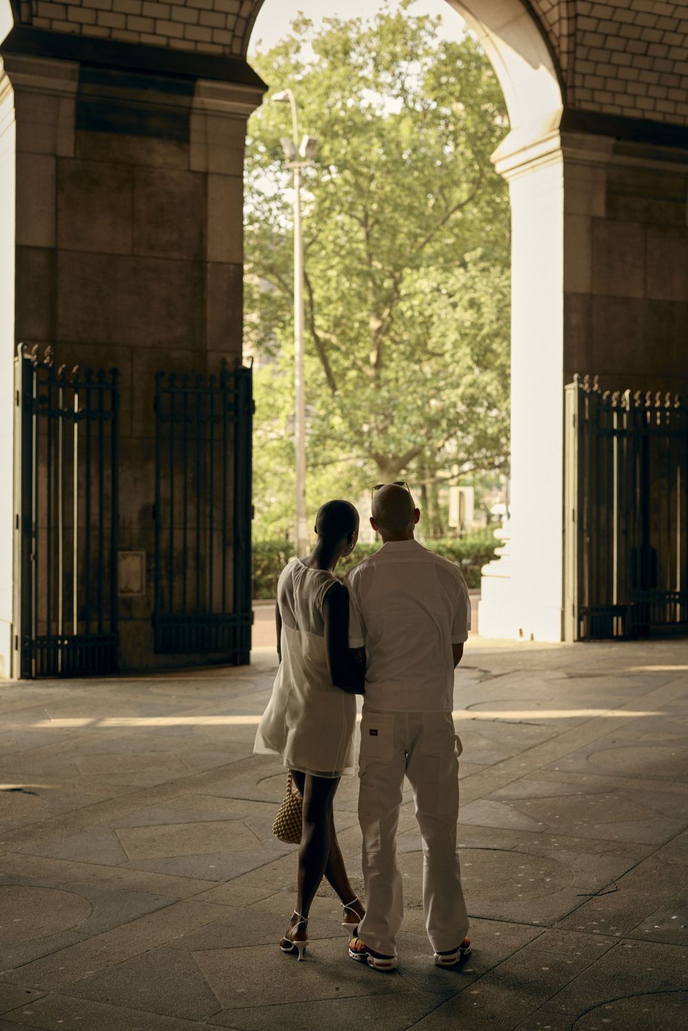 Couple standing under arched entryway looking out towards green trees.