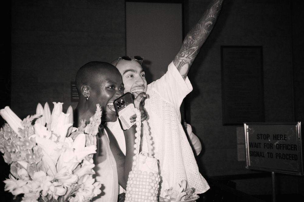 Black and white photo of celebration with raised arms and flowers in an indoor setting.