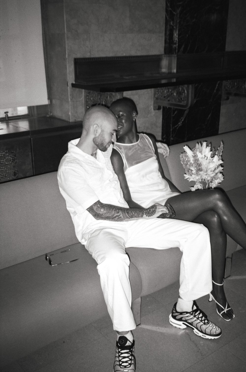 Intimate black and white photo of couple sitting close together on modern sofa.
