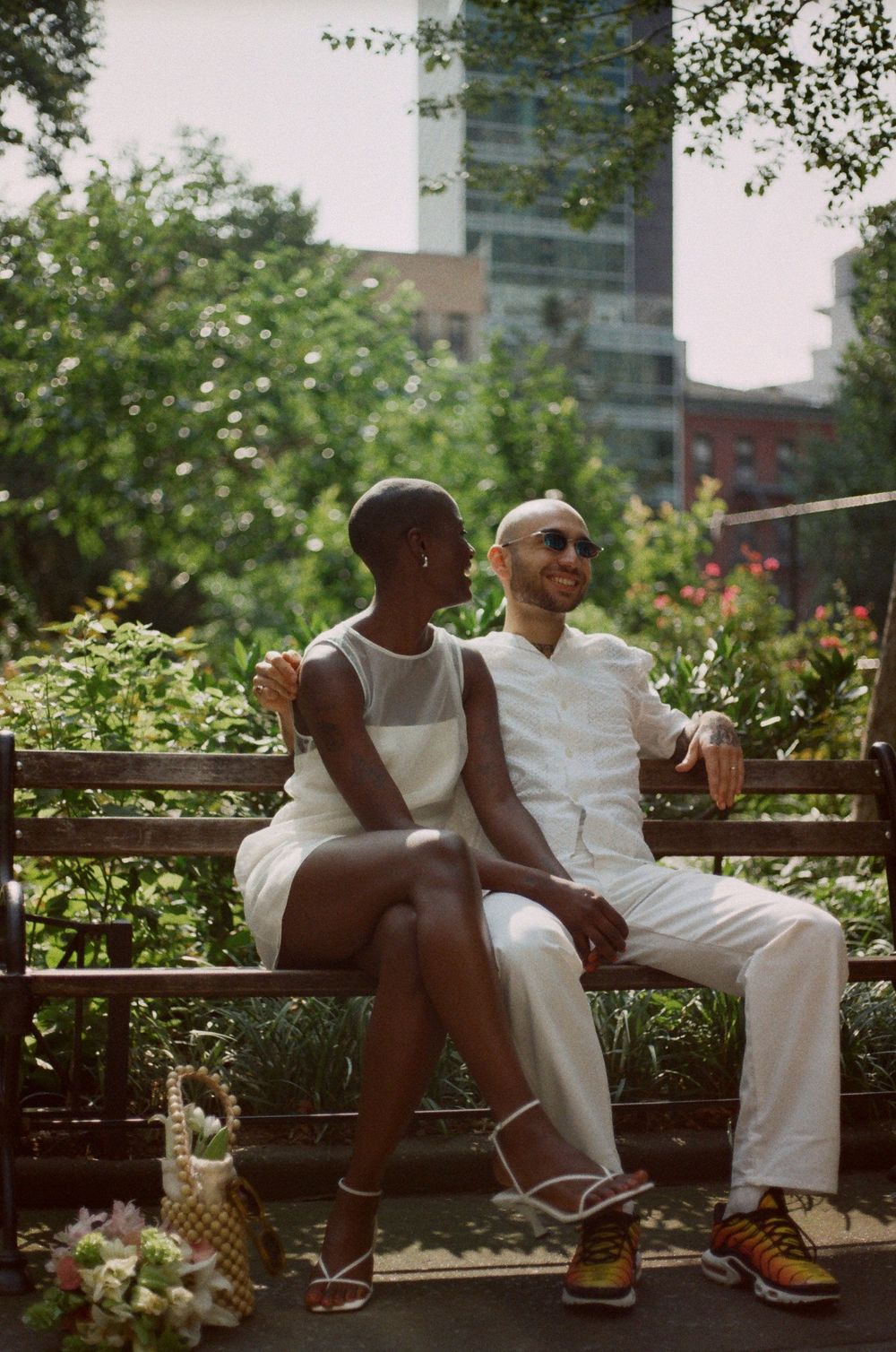 Couple in white outfits sitting together on a park bench surrounded by greenery.