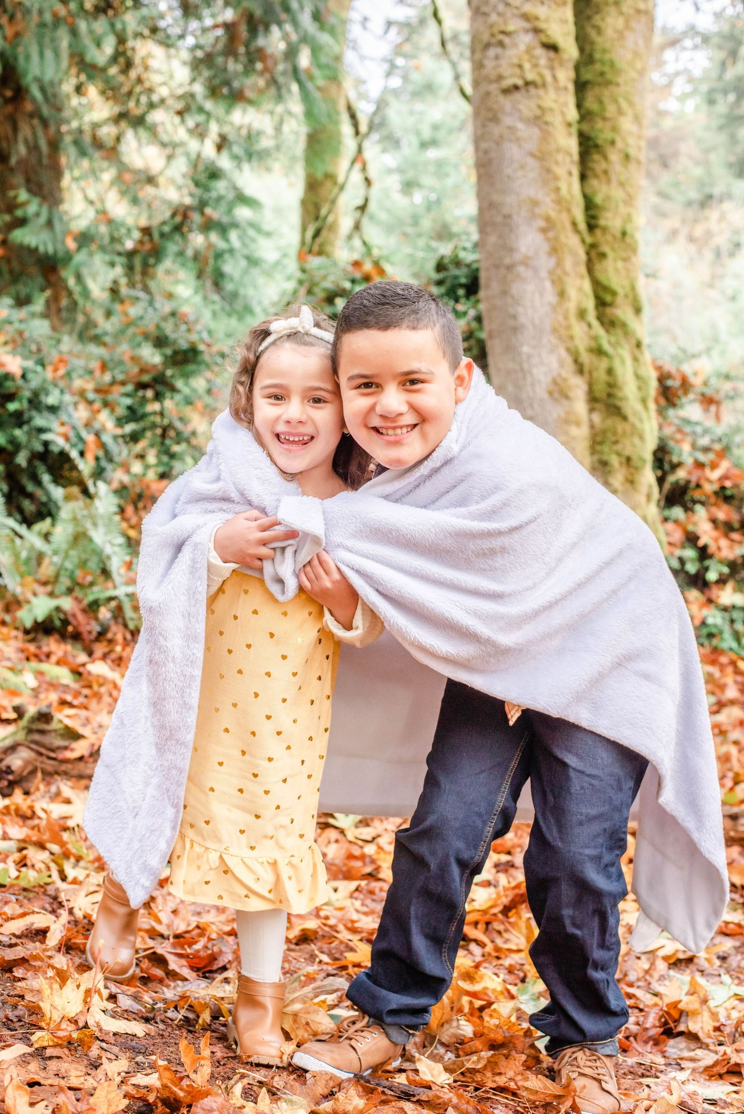 Joyful moment captured of figures playing peek-a-boo with a white blanket in autumn leaves.