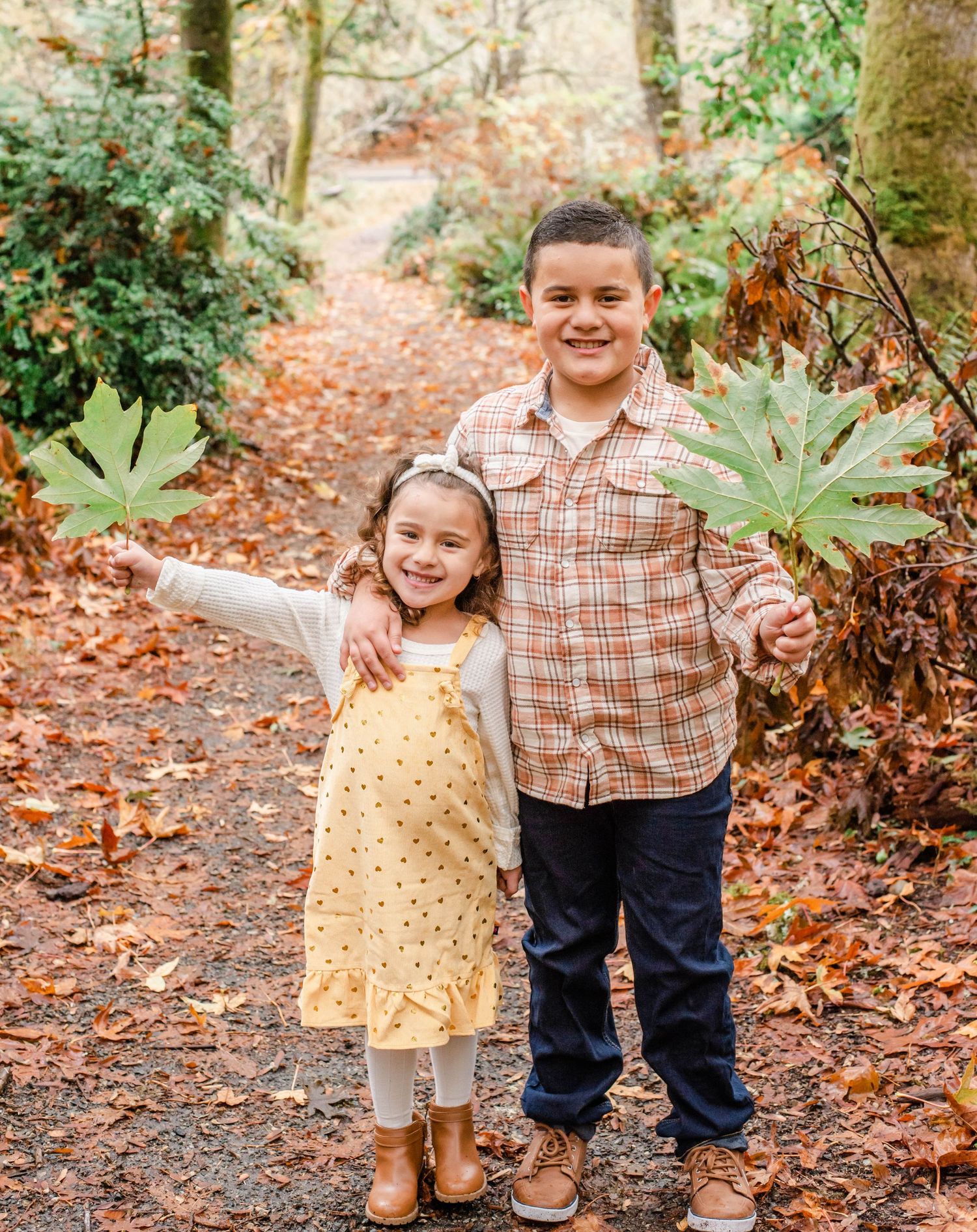 Family members pose together on forest path surrounded by autumn leaves.