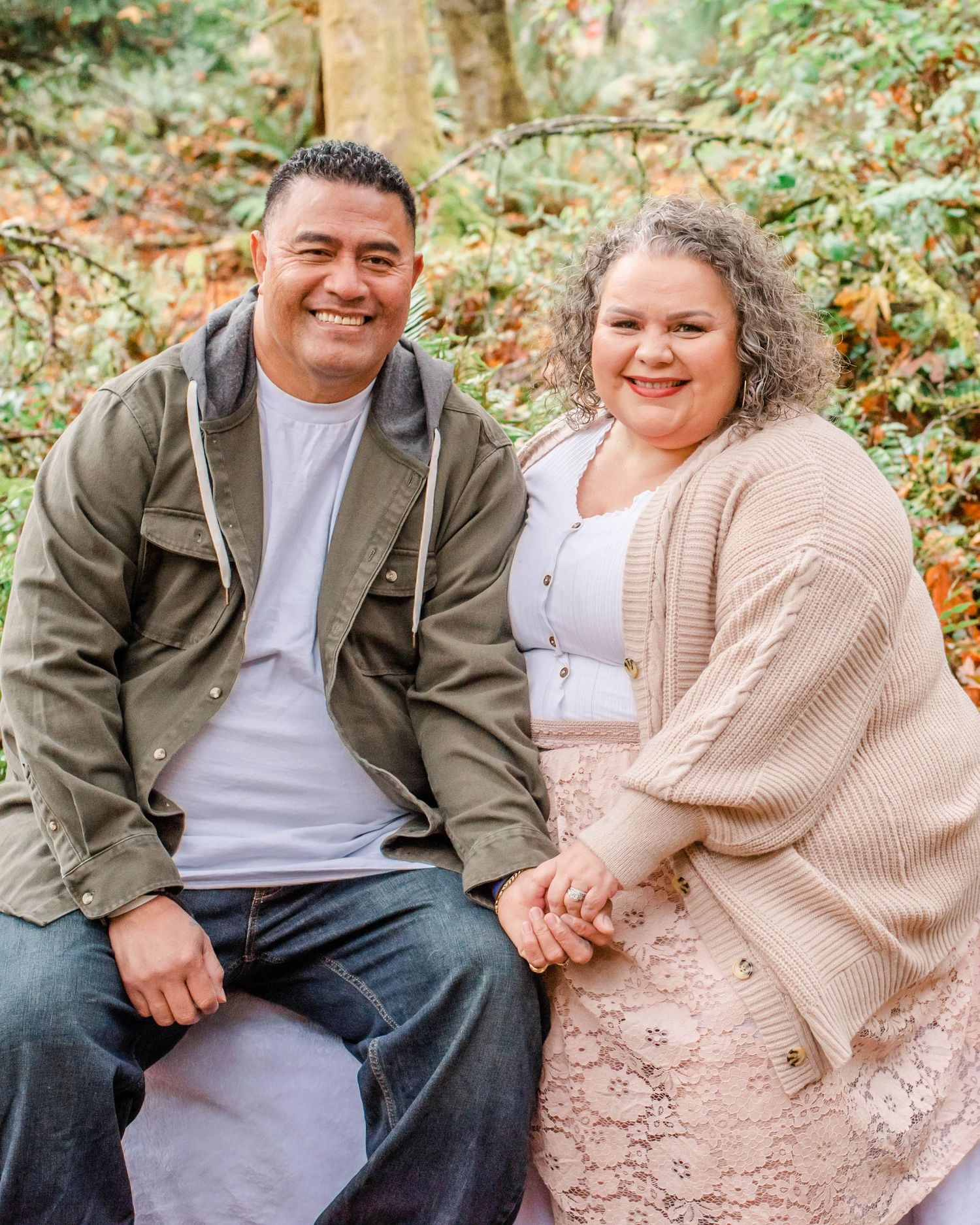 Couple sitting together on log in wooded area during autumn photoshoot.