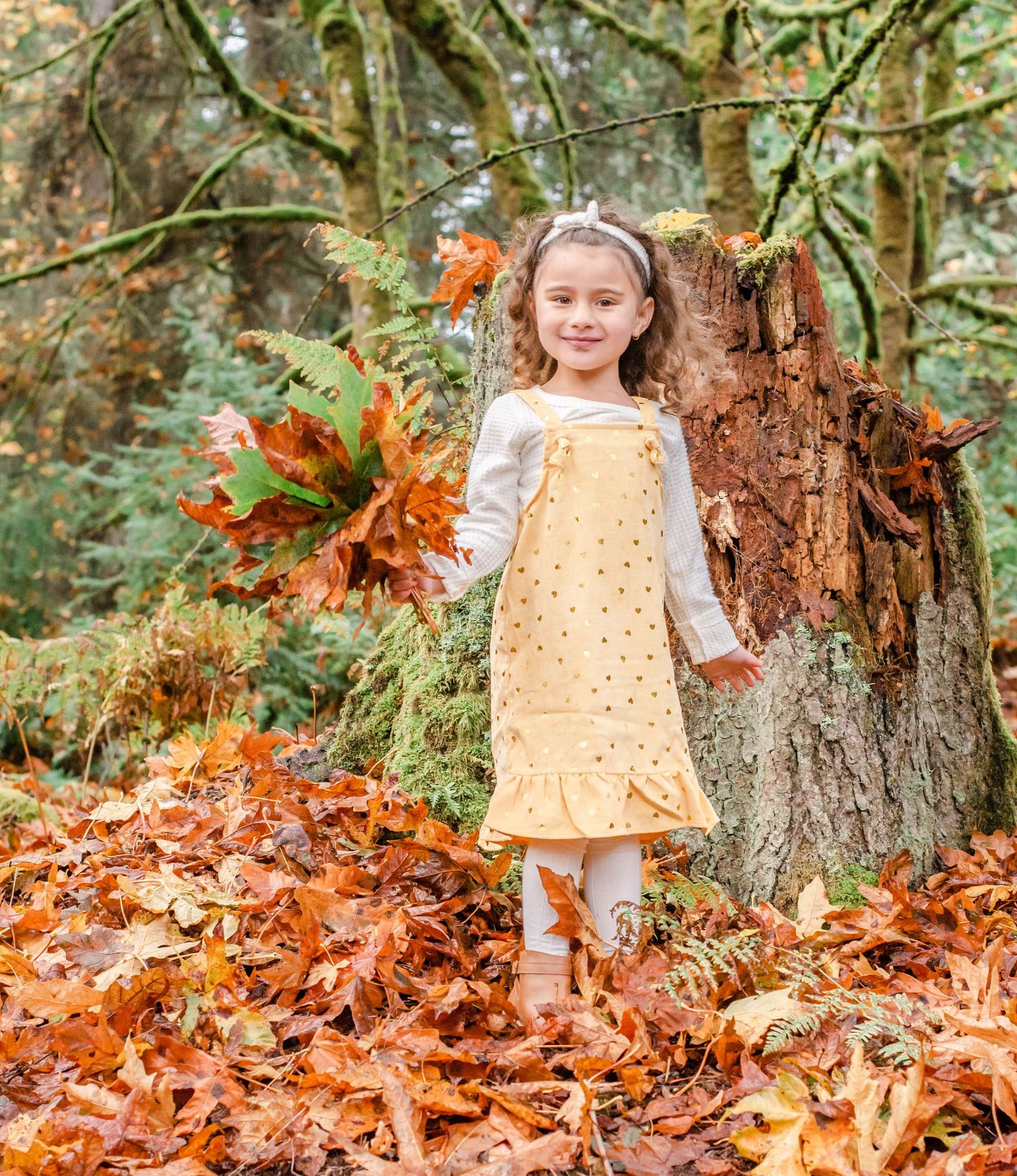 Yellow overalls stand out against rustic forest setting with scattered autumn leaves.