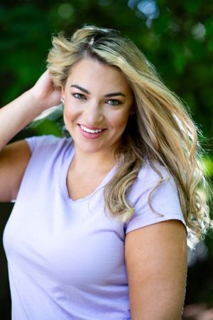 Casual outdoor portrait of a woman in purple shirt with wind-swept blonde hair.