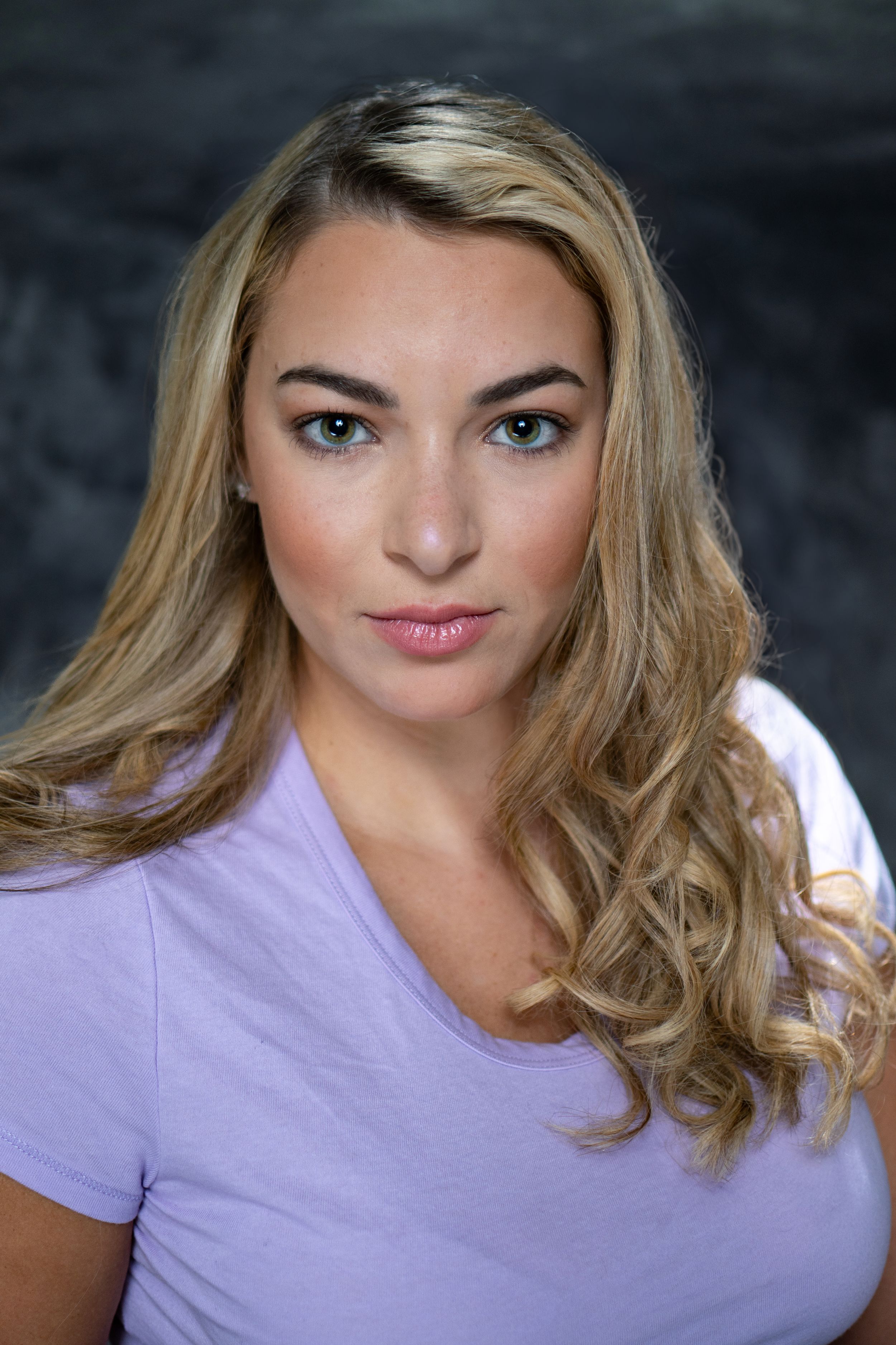 Professional headshot with purple top against dark backdrop.
