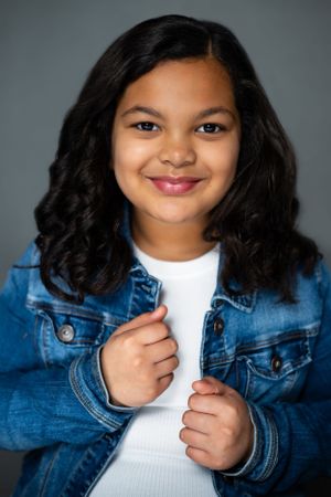 Studio portrait in denim jacket and white top with hands holding jacket lapels.