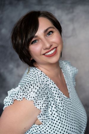 Professional portrait of someone wearing a polka dot blouse with ruffled sleeves against a gray backdrop.