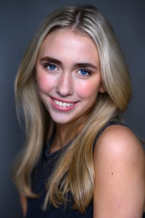 Studio portrait of a blonde model with bright blue eyes smiling at camera.
