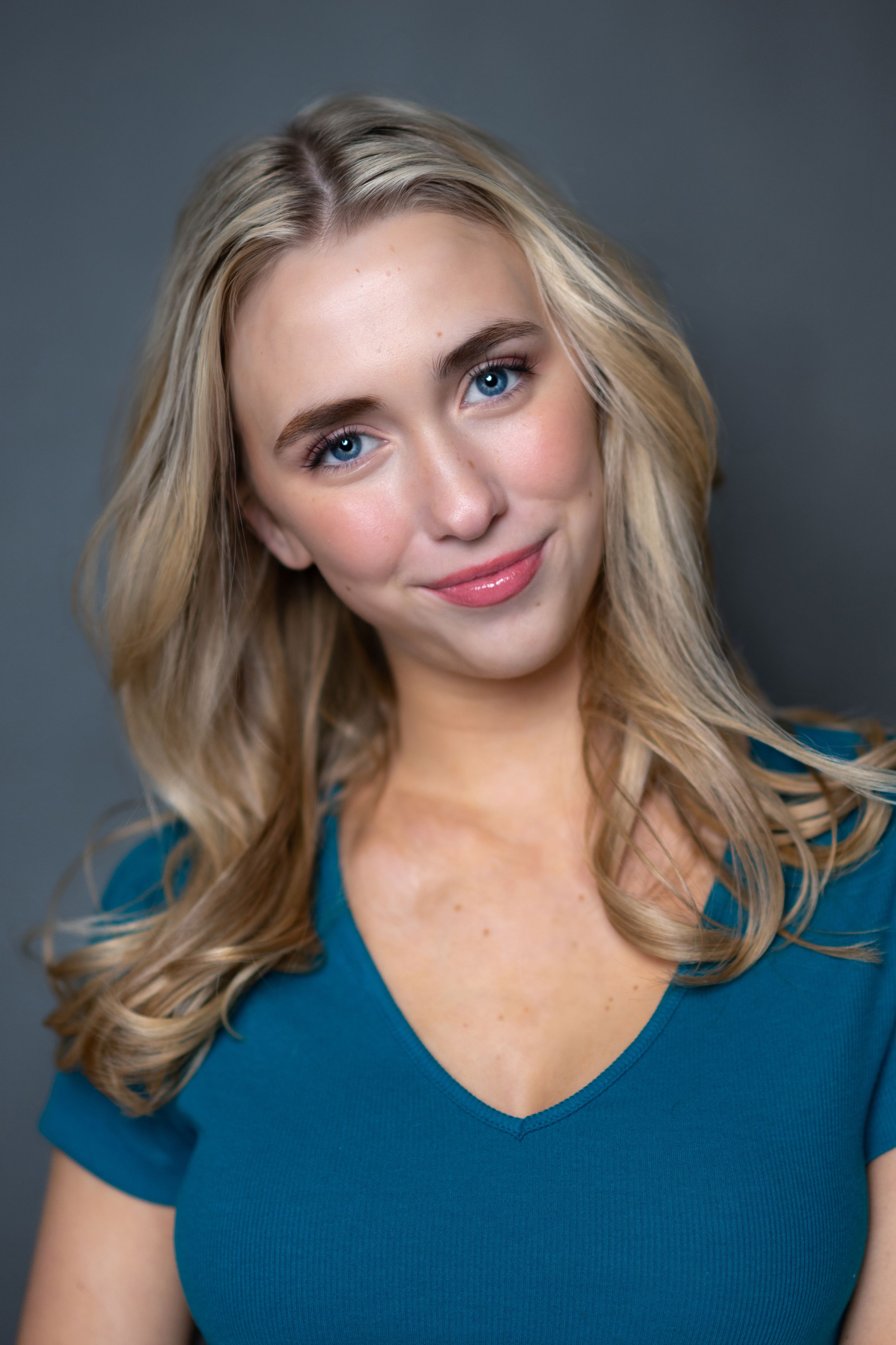 Professional headshot of woman in teal top against grey backdrop.