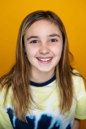 Portrait against yellow background showing bright smile and tie-dye shirt.