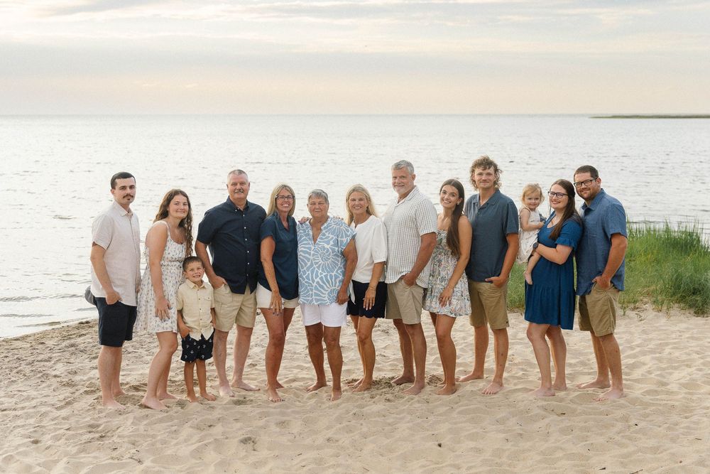 Large family group posing together on sandy beach at sunset.